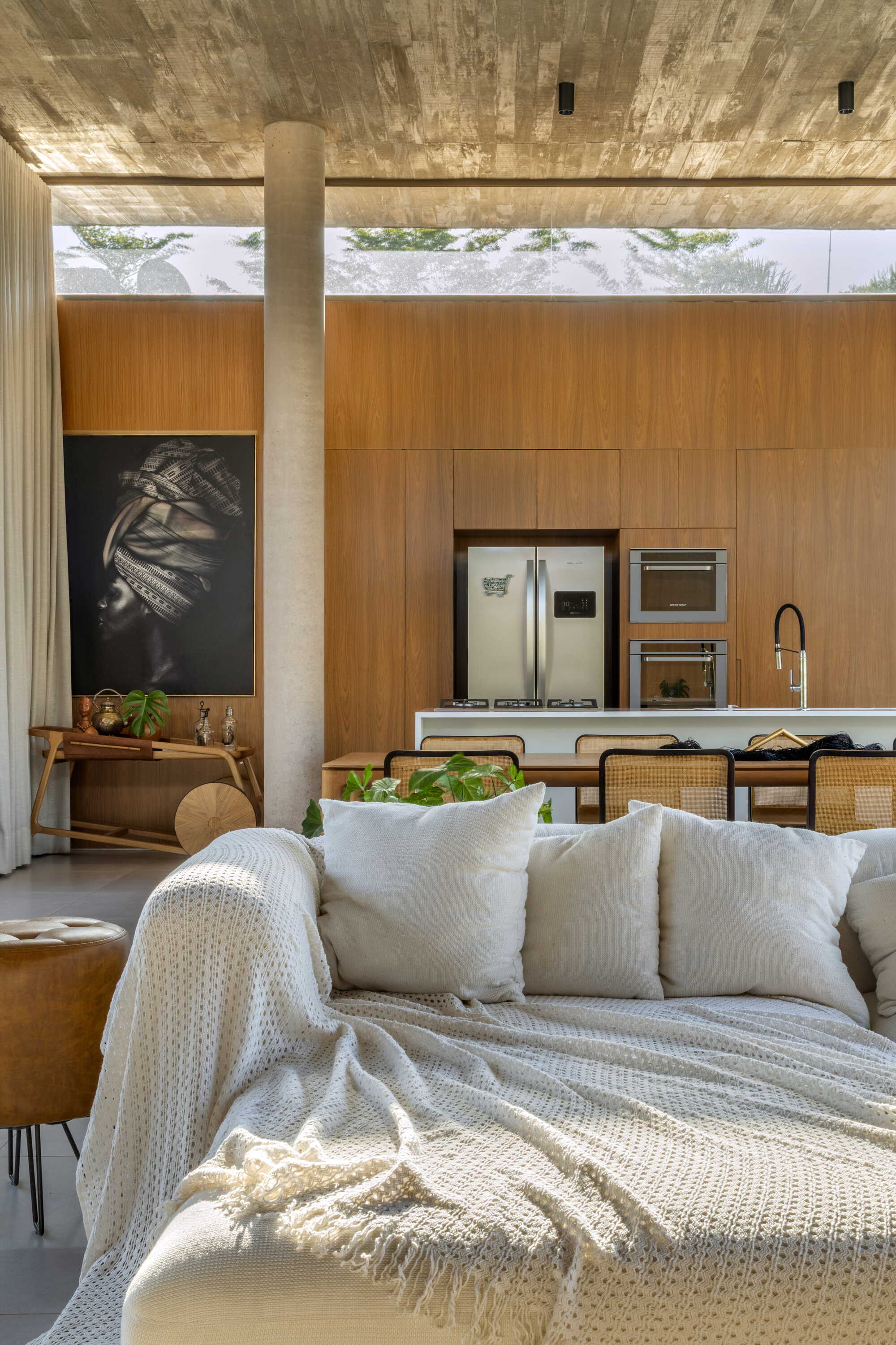 Board-formed concrete column beside the kitchen island and wood-paneled wall with clerestory window above