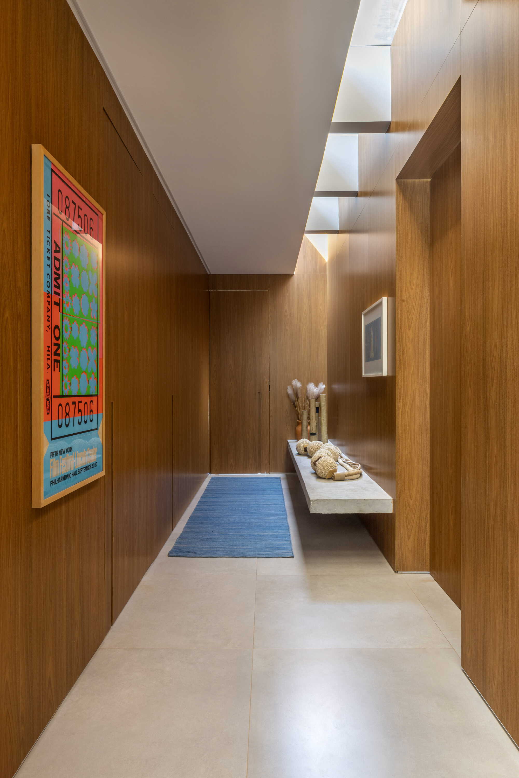 Narrow hallway with wood paneled walls, recessed ceiling lighting and pale stone floor