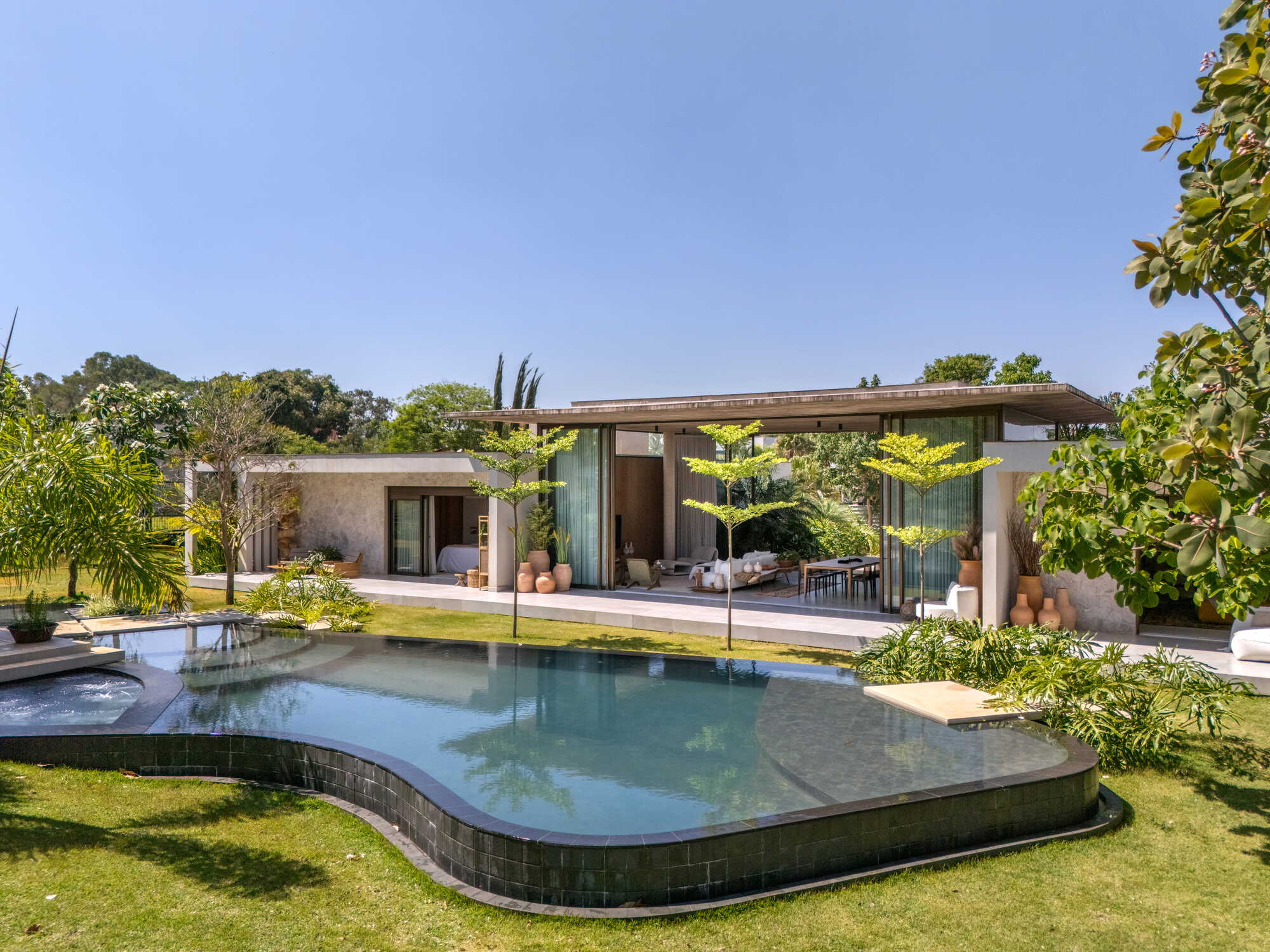 Raised pool with curved edges and glass fence facing a low pavilion under mature trees