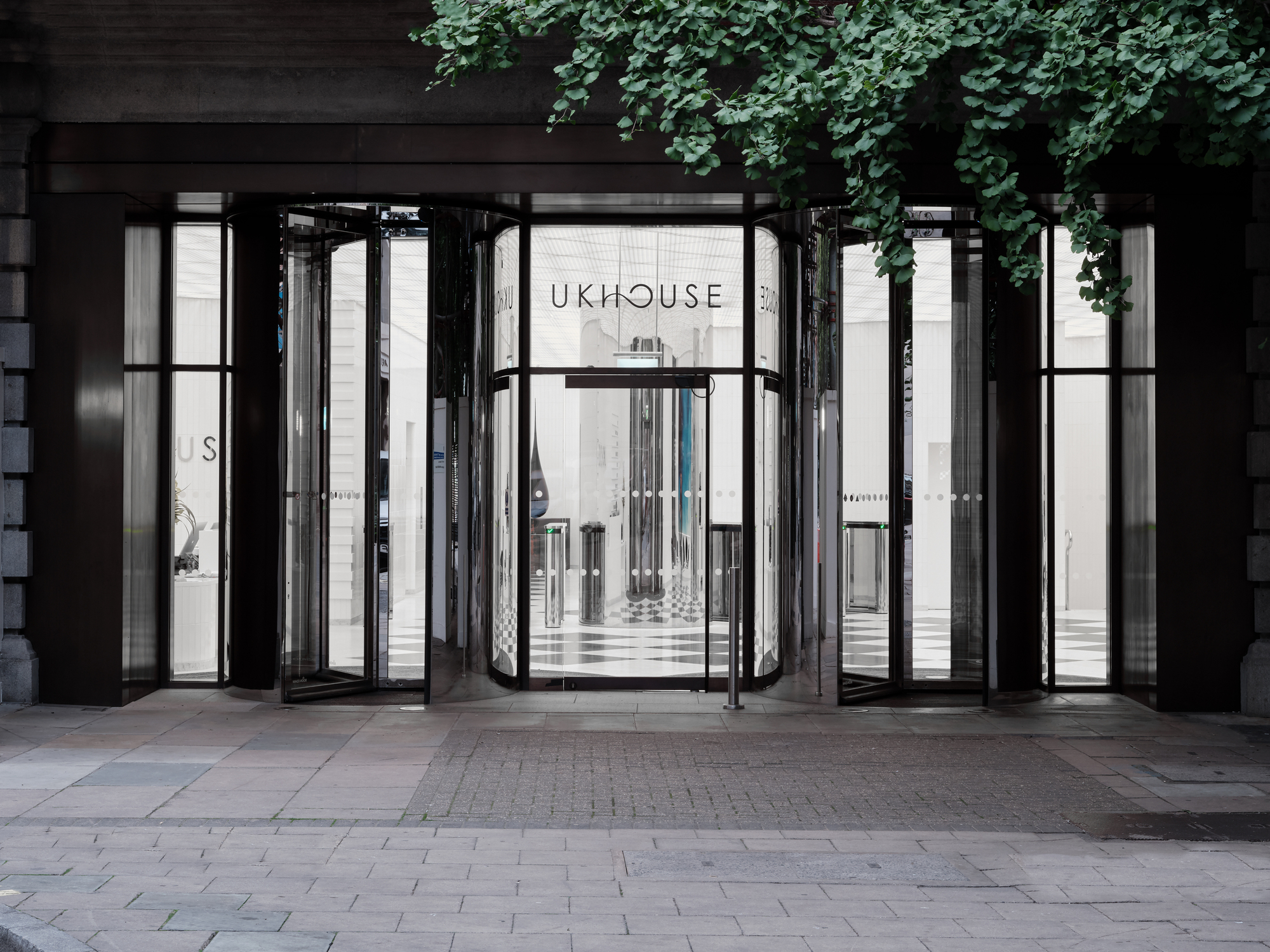 Street view of the glass folding door entrance framed by dark metal and overhanging ivy