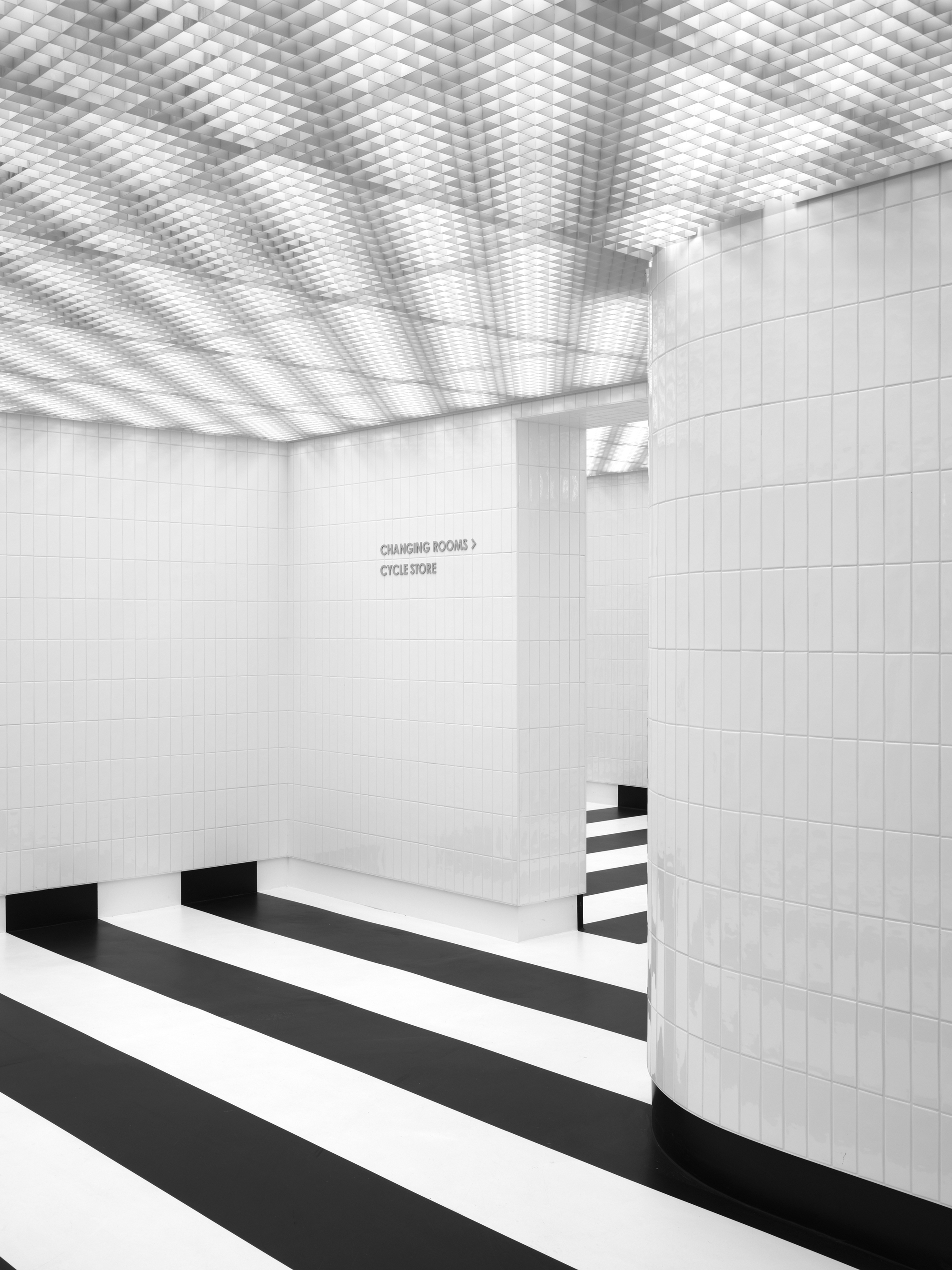 White tiled corner with wayfinding signage near a stepped platform under patterned light