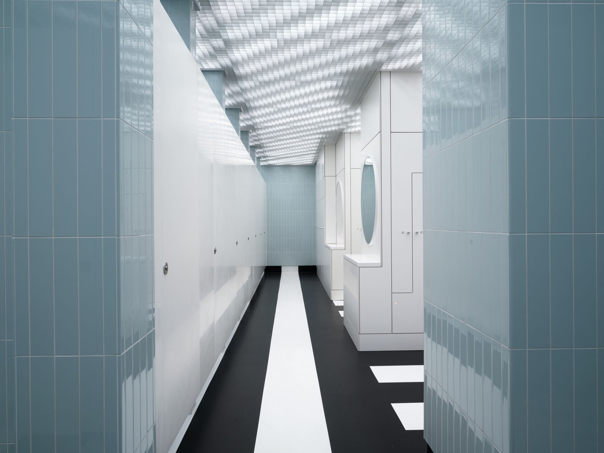 Interior corridor with blue tile walls, black and white striped floor beneath a grid ceiling skylight
