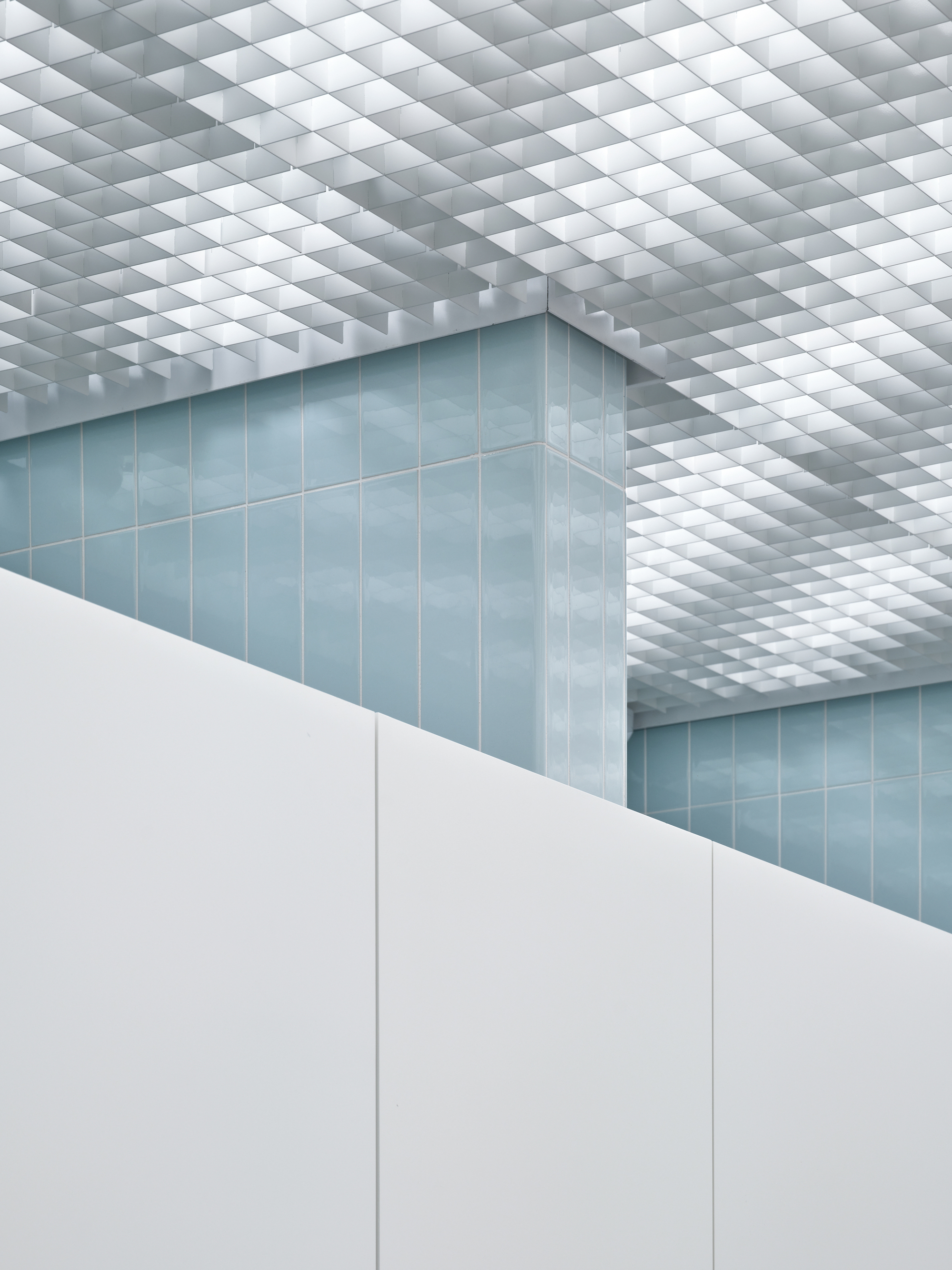 Corner view of blue tiled wall beneath a white pyramidal grid ceiling