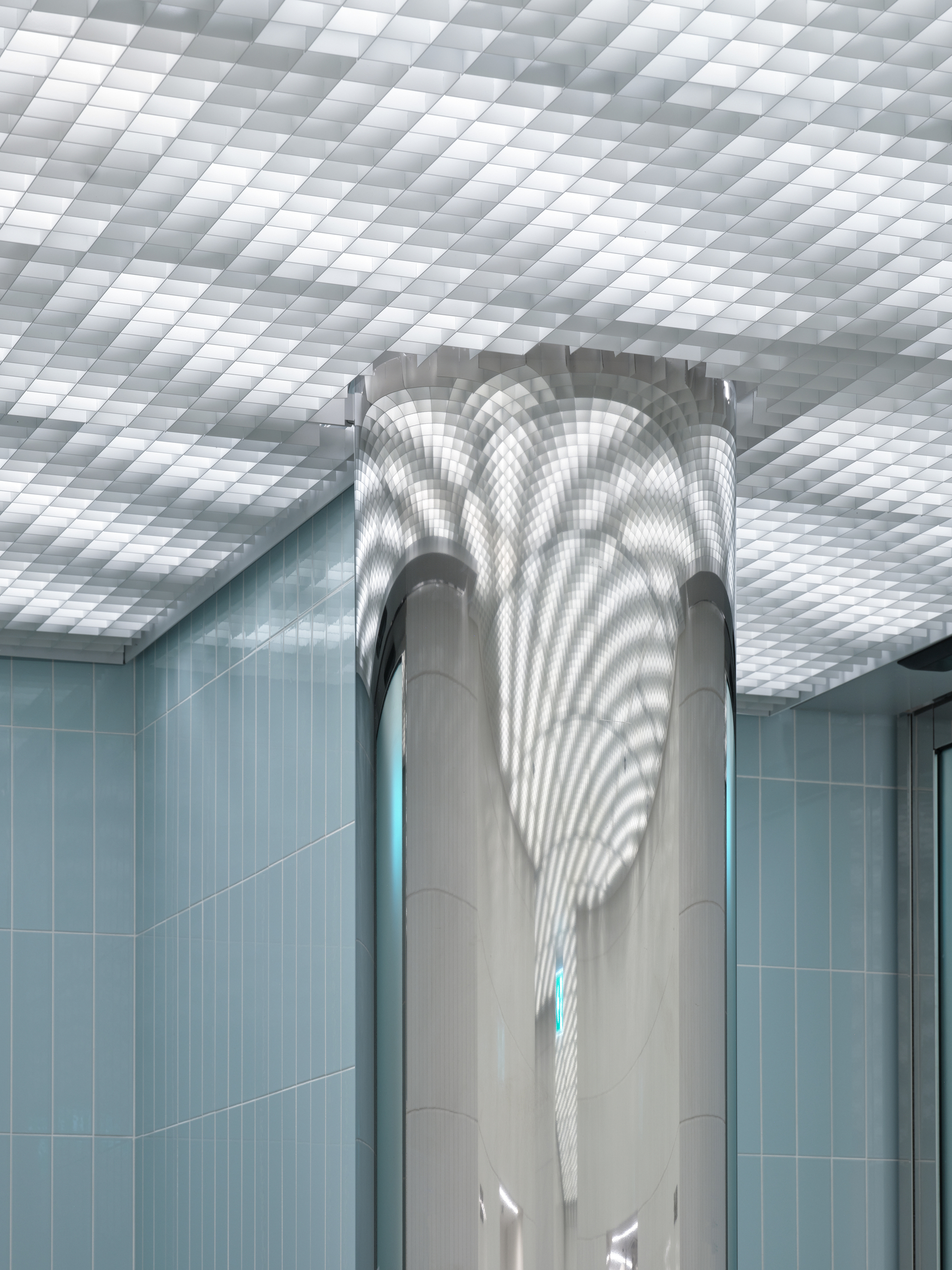 Central column wrapped in smooth paneling beneath a coffered translucent ceiling with light blue tiled walls