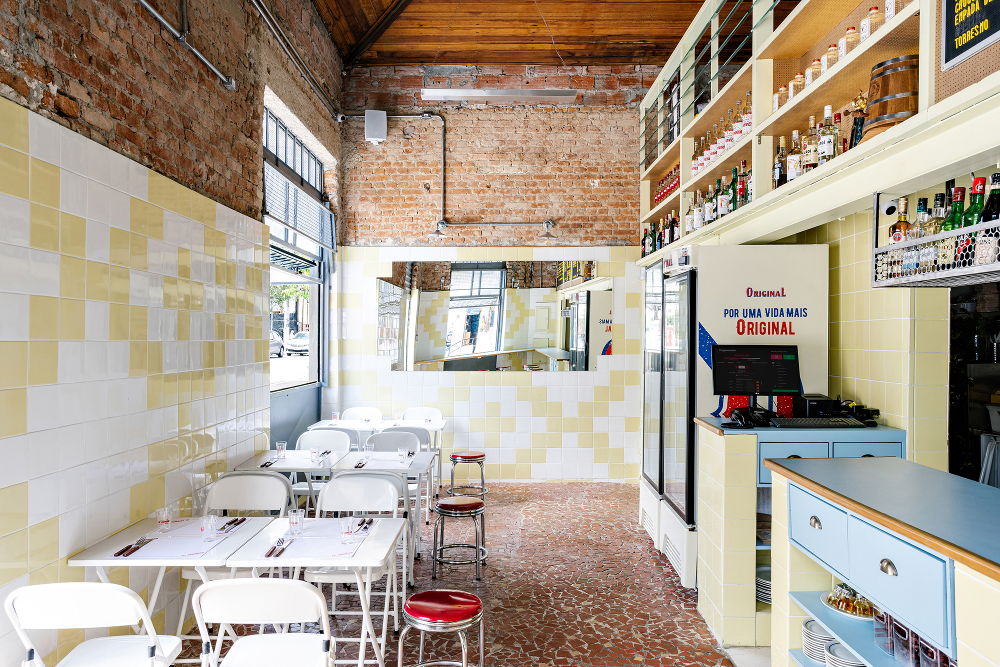 Interior view of a dining area with exposed brick walls, yellow and white checkerboard tile and white tables