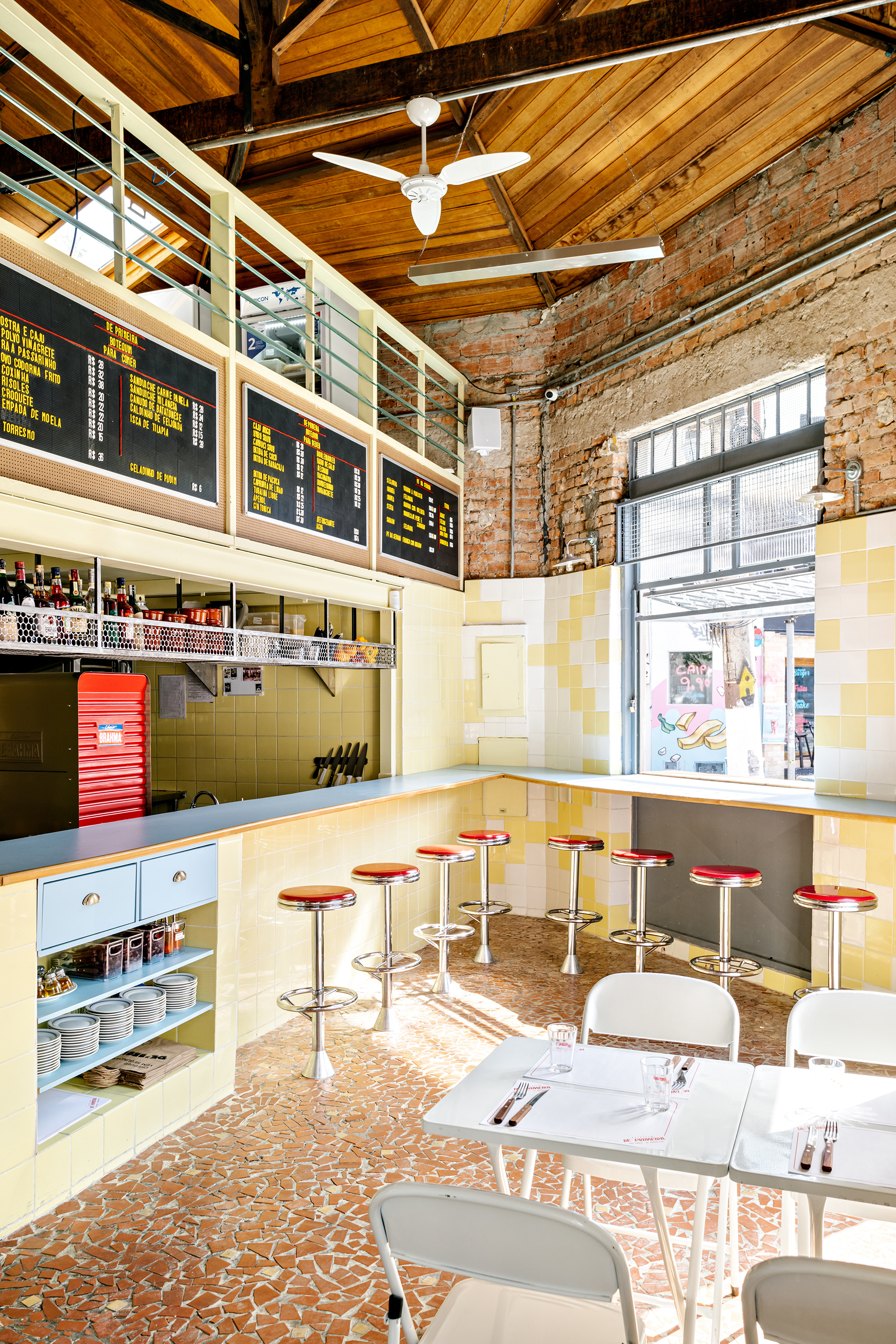 Dining space with timber ceiling, yellow tile walls, red bar stools and digital menu boards above the counter