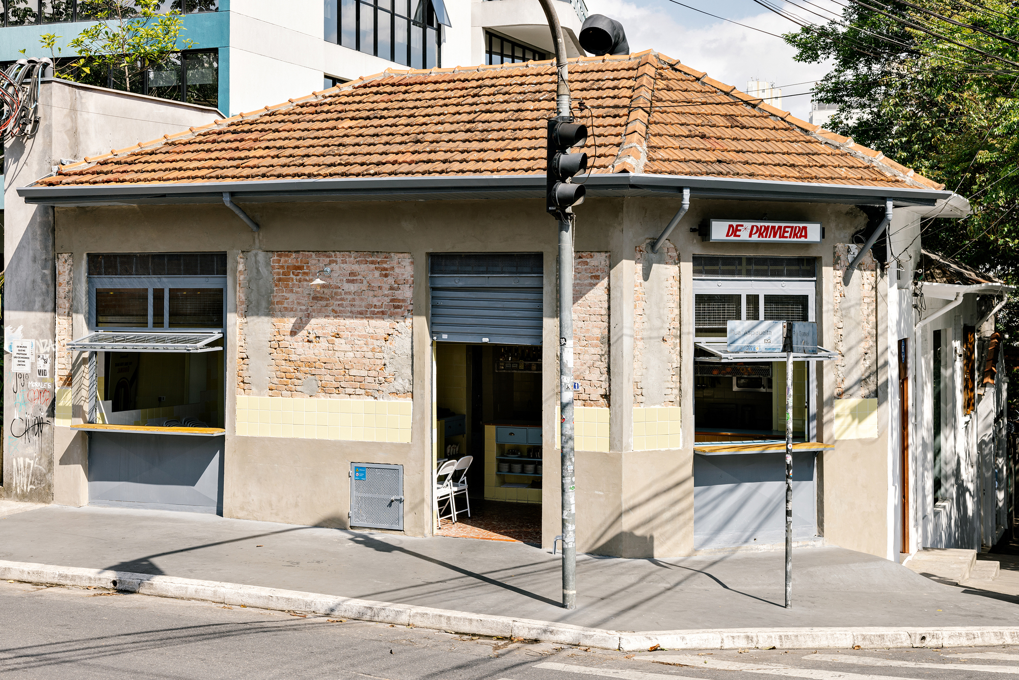 Street corner facade with terracotta tile roof, exposed brick and recessed entry under dappled tree shadows