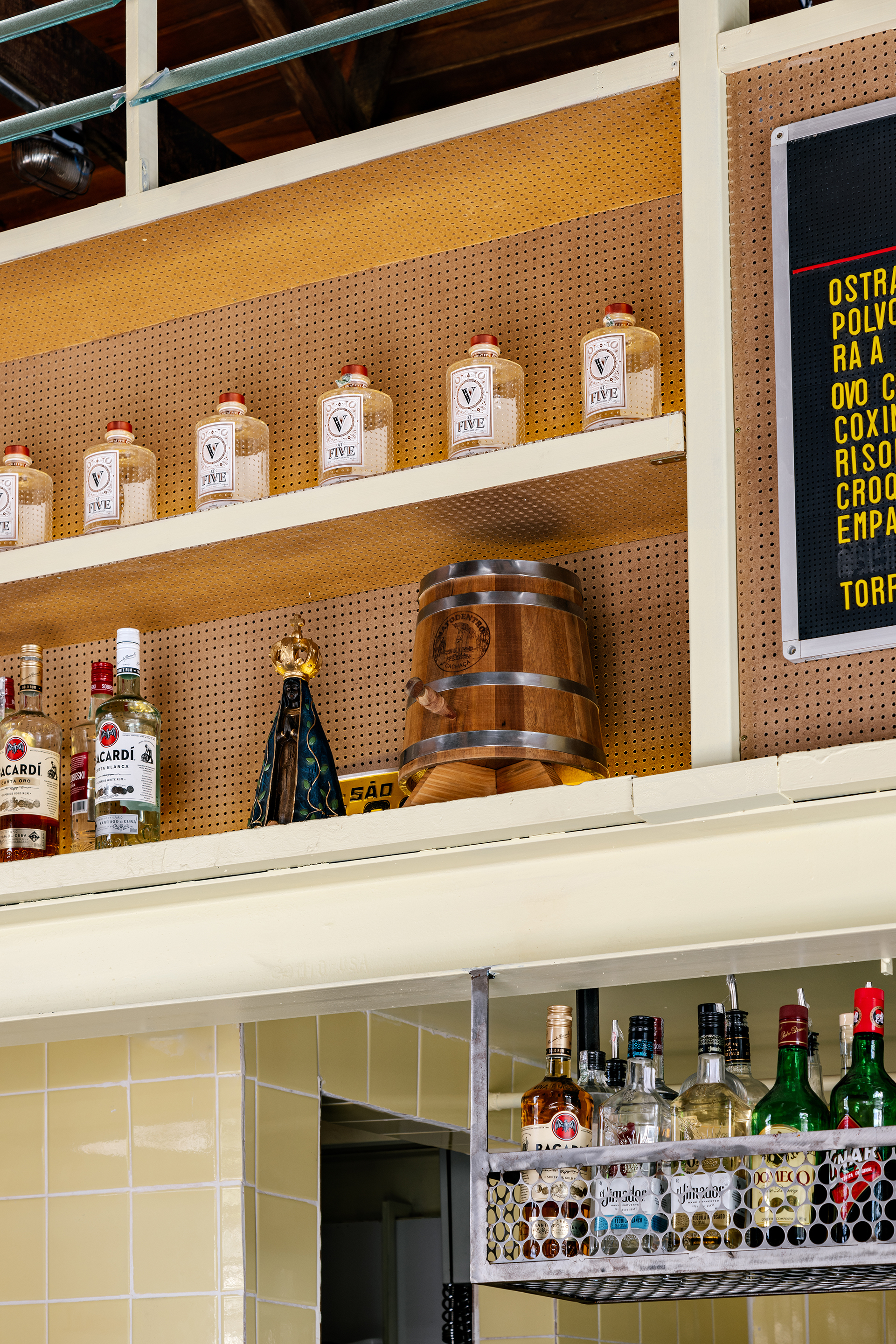 Detail of pegboard shelving with glass jars and wooden barrel beneath digital menu screen