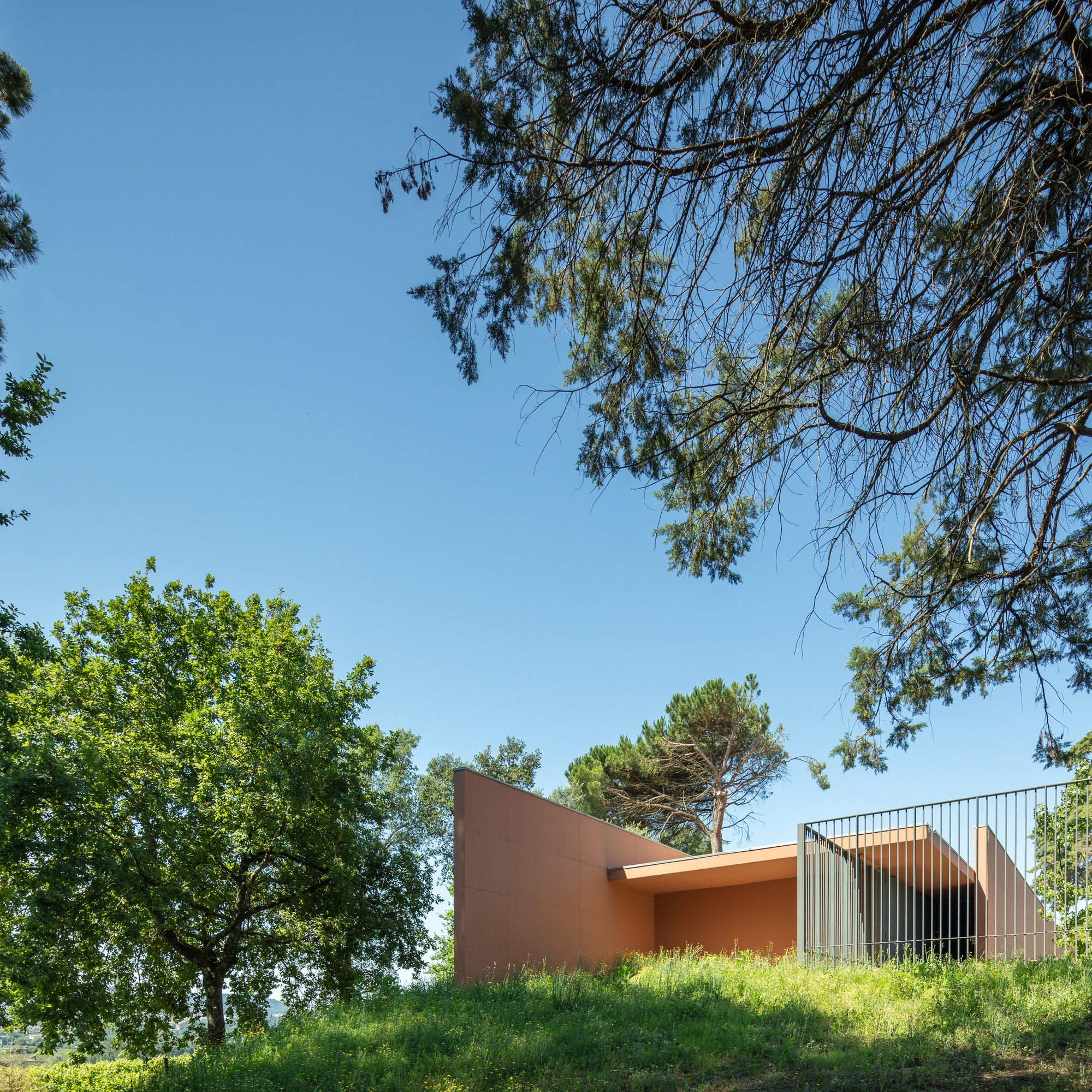 Terracotta walls and vertical metal screening atop a naturalized berm under deciduous and pine trees