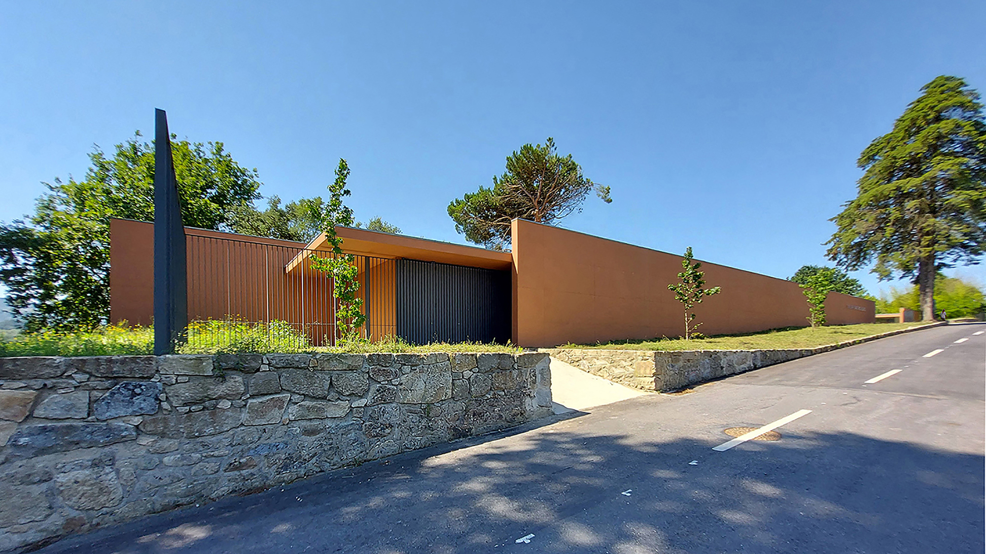 Street view showing the terracotta facade with recessed entry and vertical screening above a stacked stone retaining wall