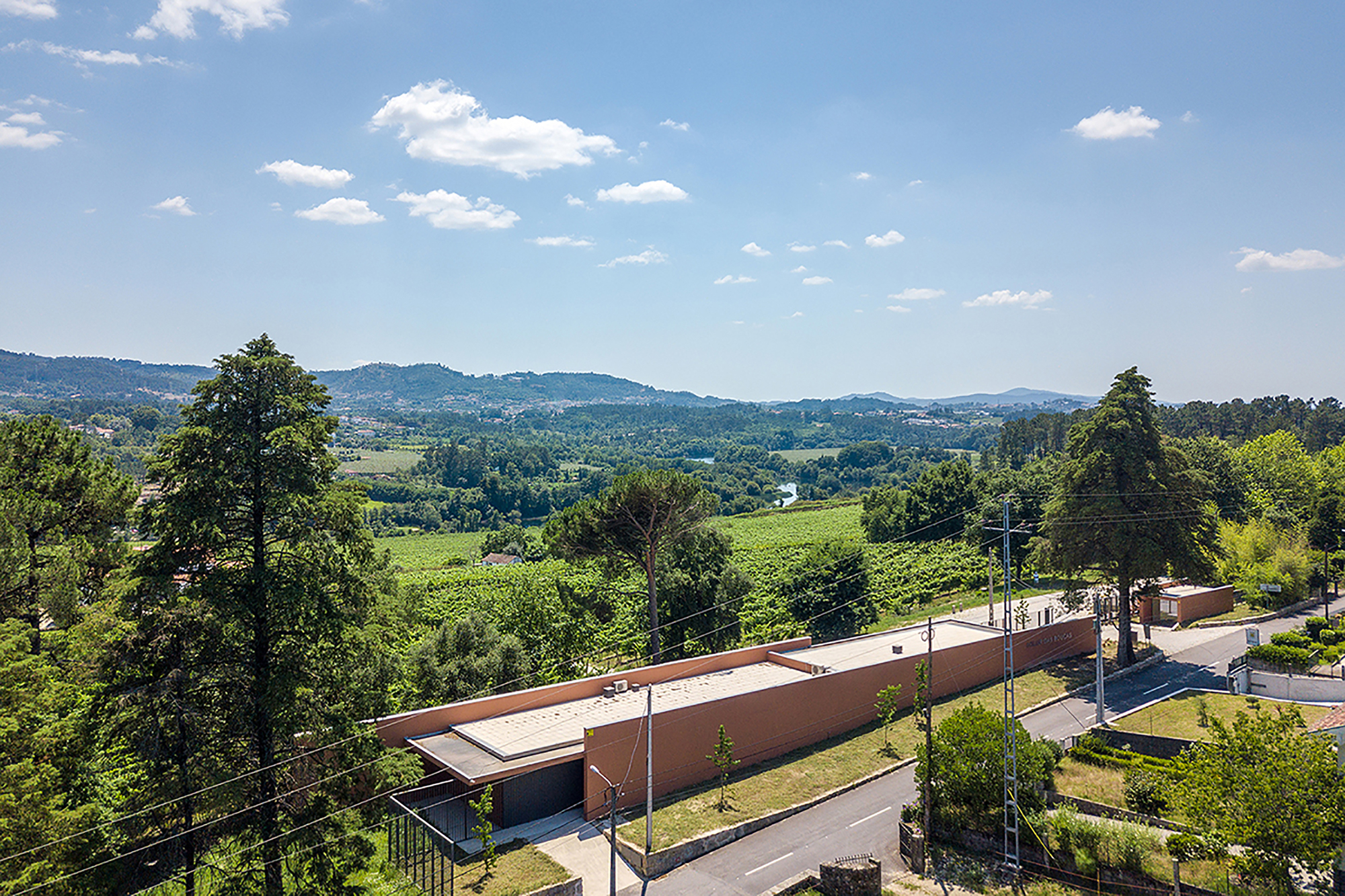Aerial view of the low terracotta-roofed structure set along a road with vineyards and hills beyond
