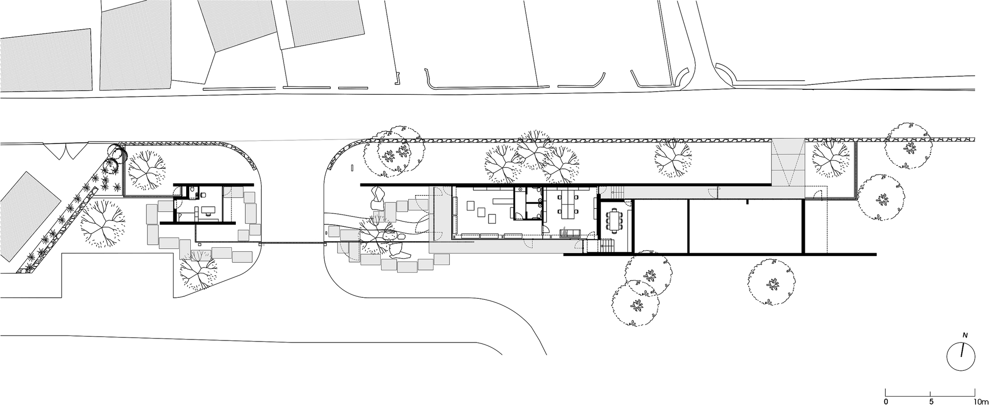 Site plan drawing showing a linear building with curved pathways and trees indicated in the landscape