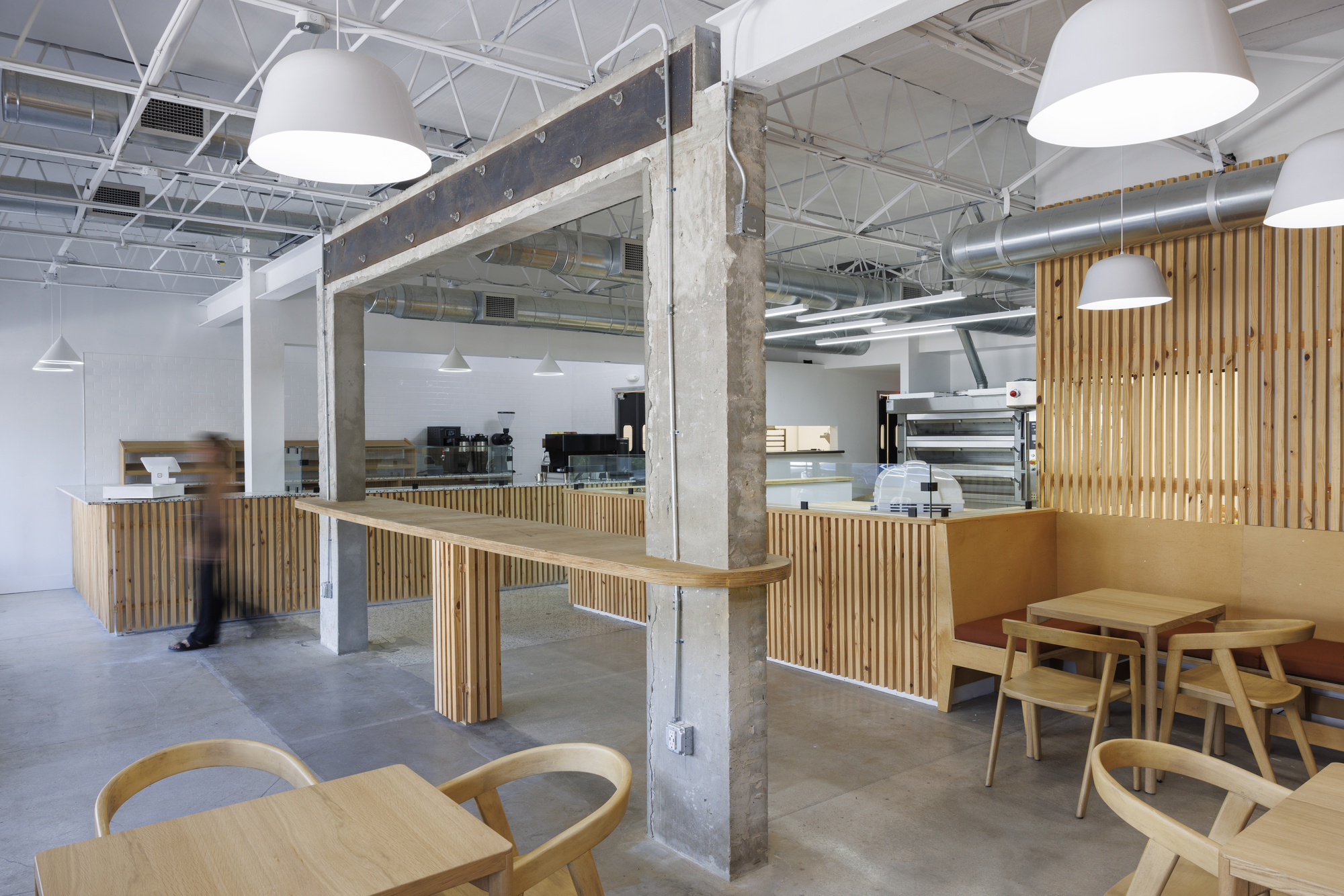 Bakery interior with vertical timber slat counters and exposed concrete columns beneath white pendant lights