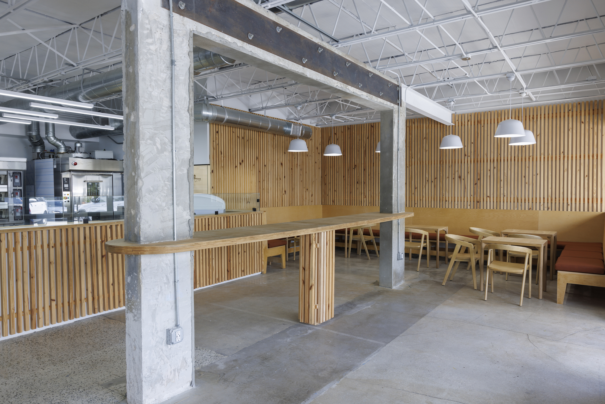Long communal timber table wrapping around a concrete column with exposed truss ceiling above