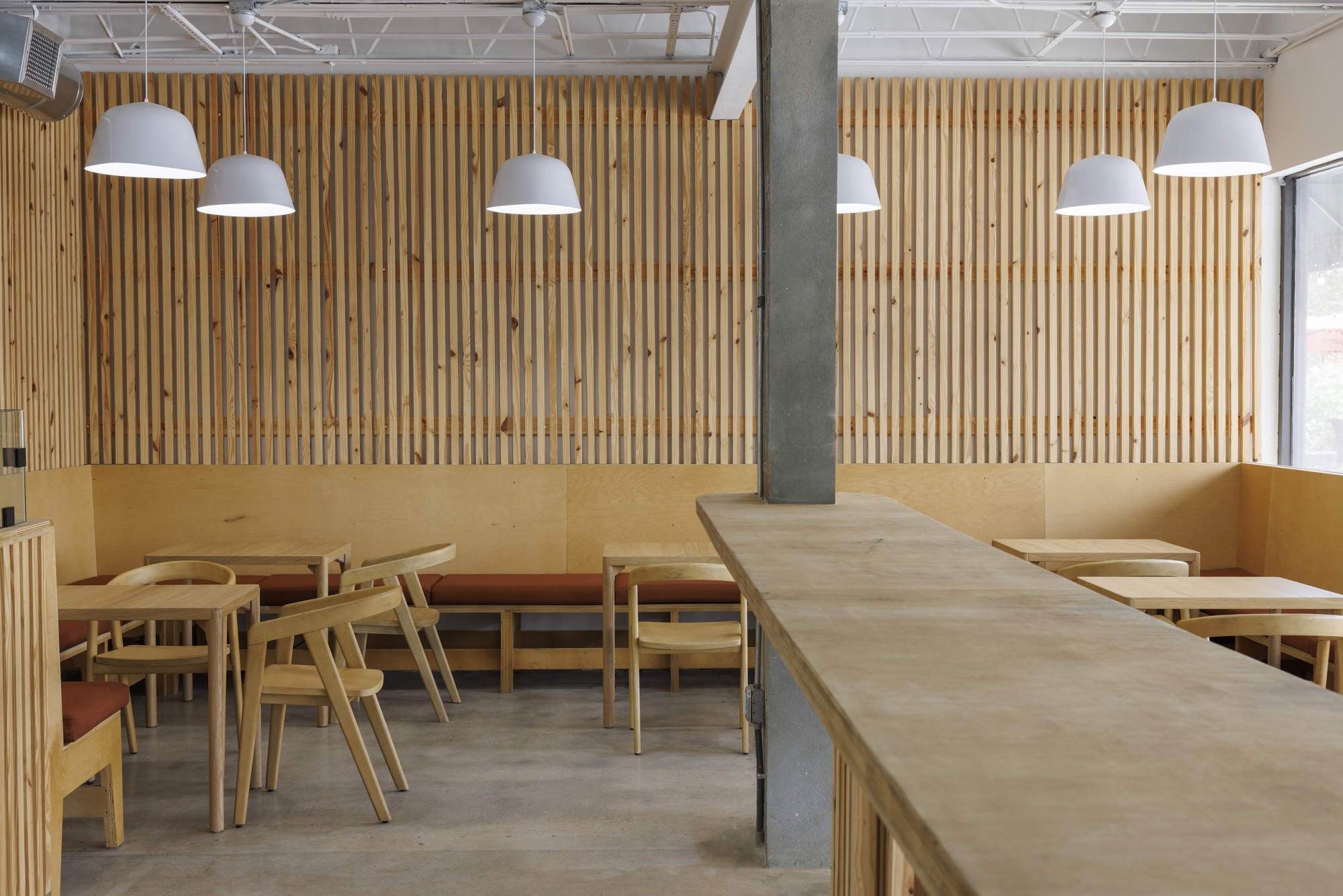 Dining area with banquette seating against vertical timber slat wall and concrete column in foreground
