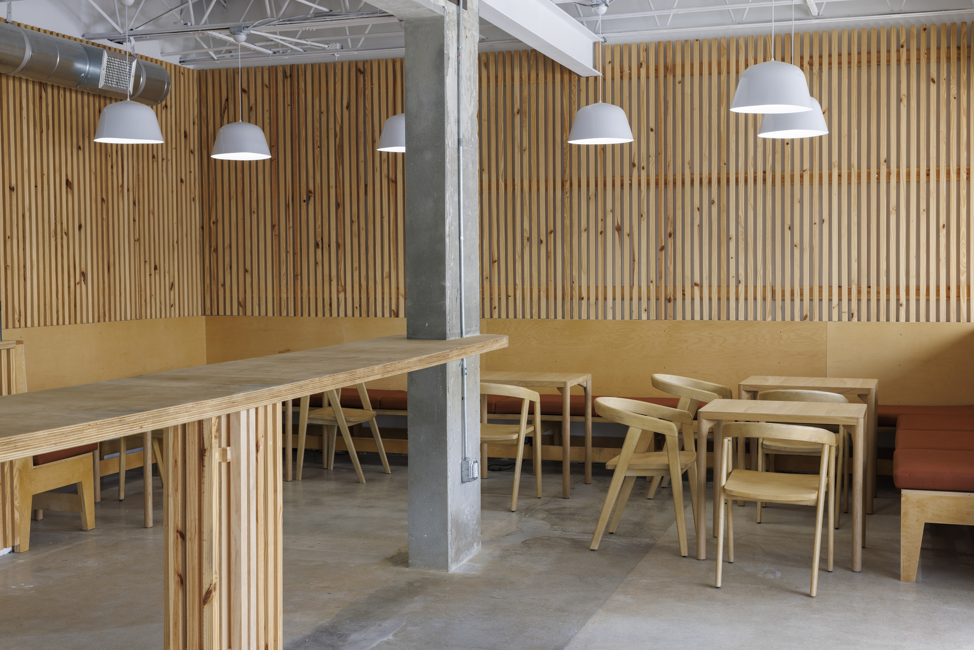 Seating zone with timber tables and chairs arranged around a raw concrete column