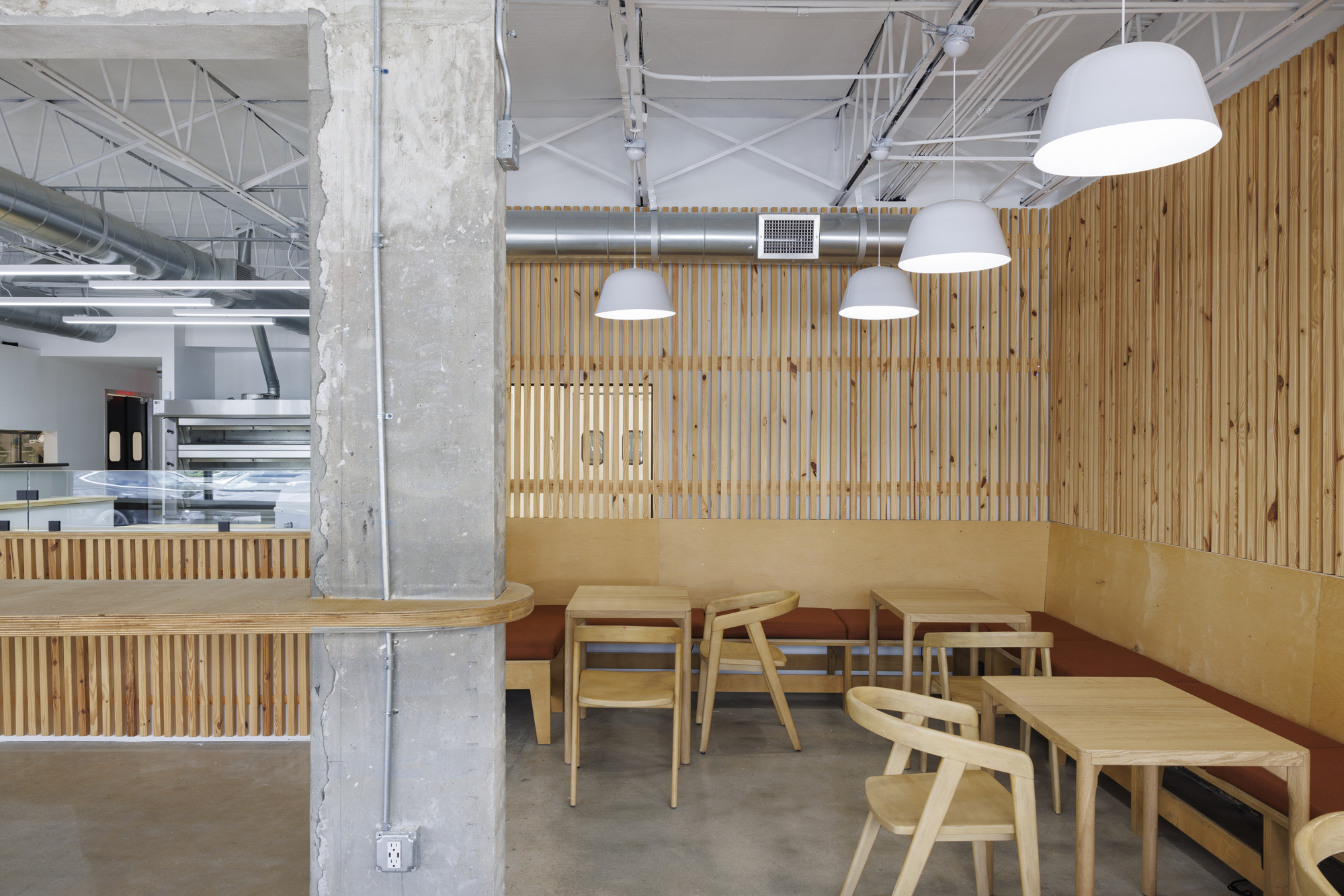 Booth seating with plywood banquette and timber chairs beneath vertical slat wall with backlit opening
