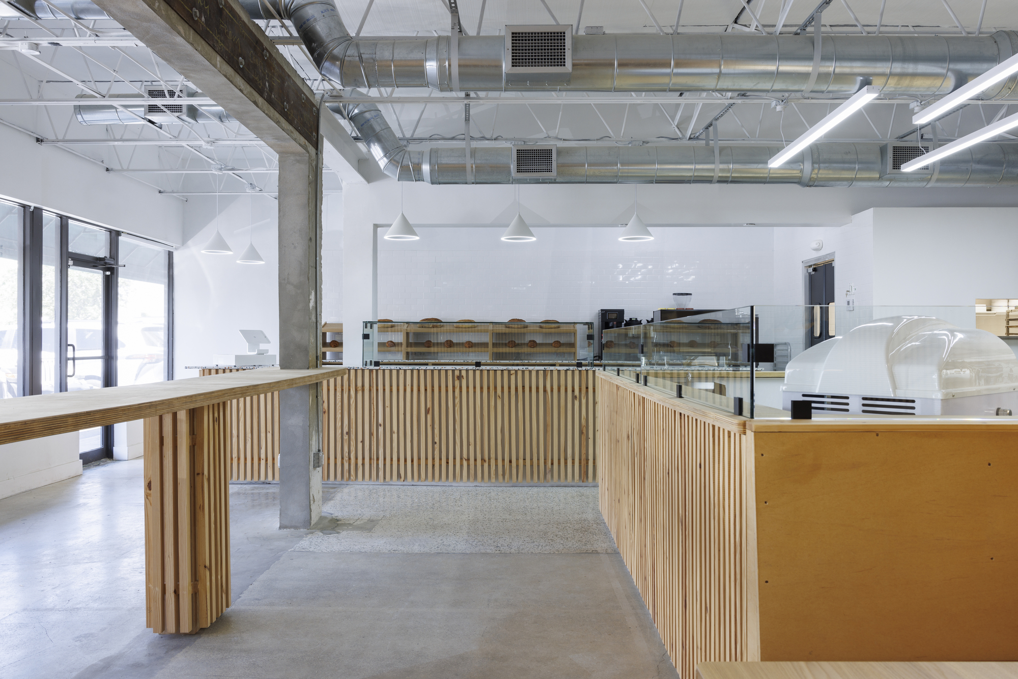 Service counter with vertical timber slat cladding and concrete floor under linear pendant lights
