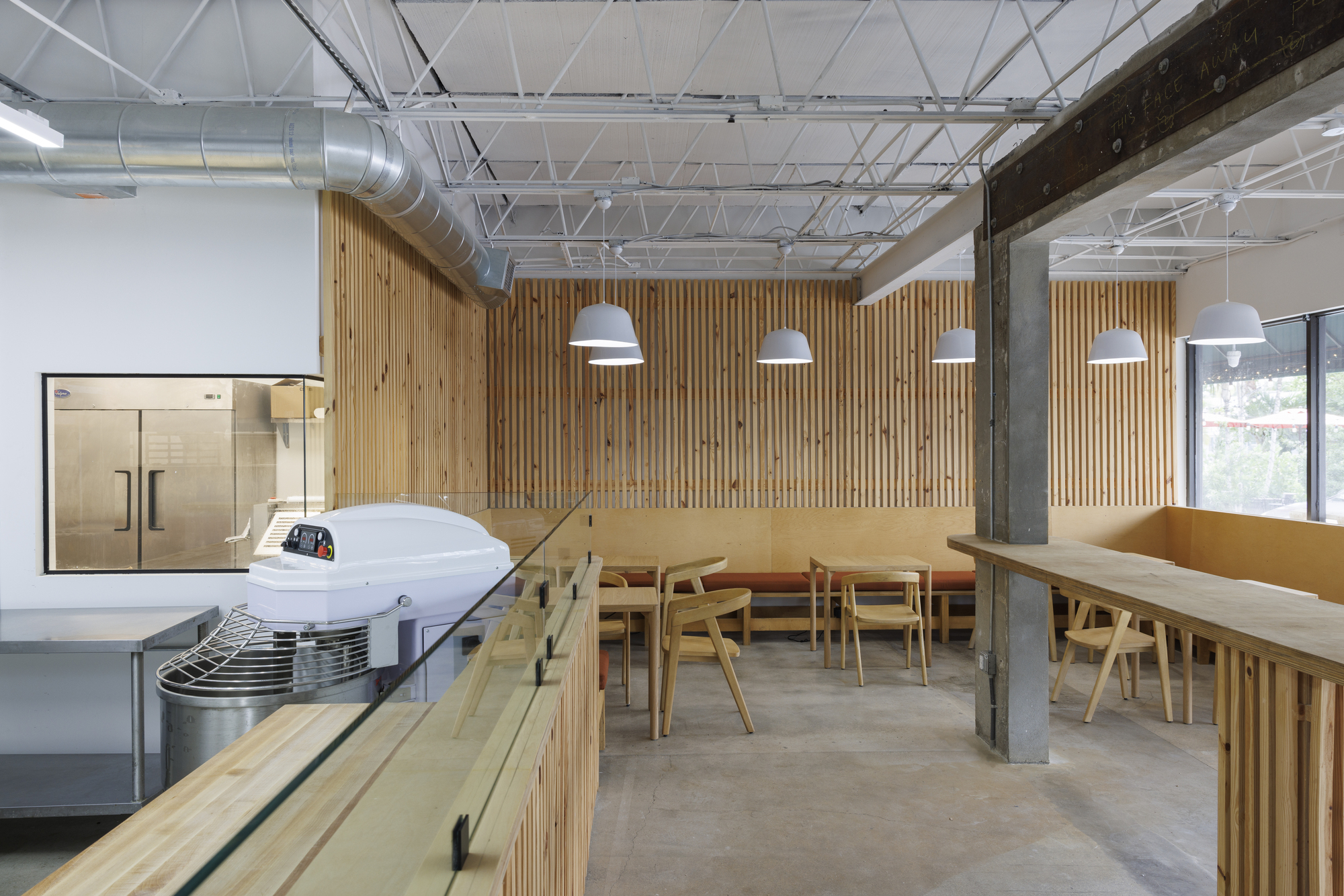 Dining area with timber tables and benches against a vertical slat wall beneath exposed structure