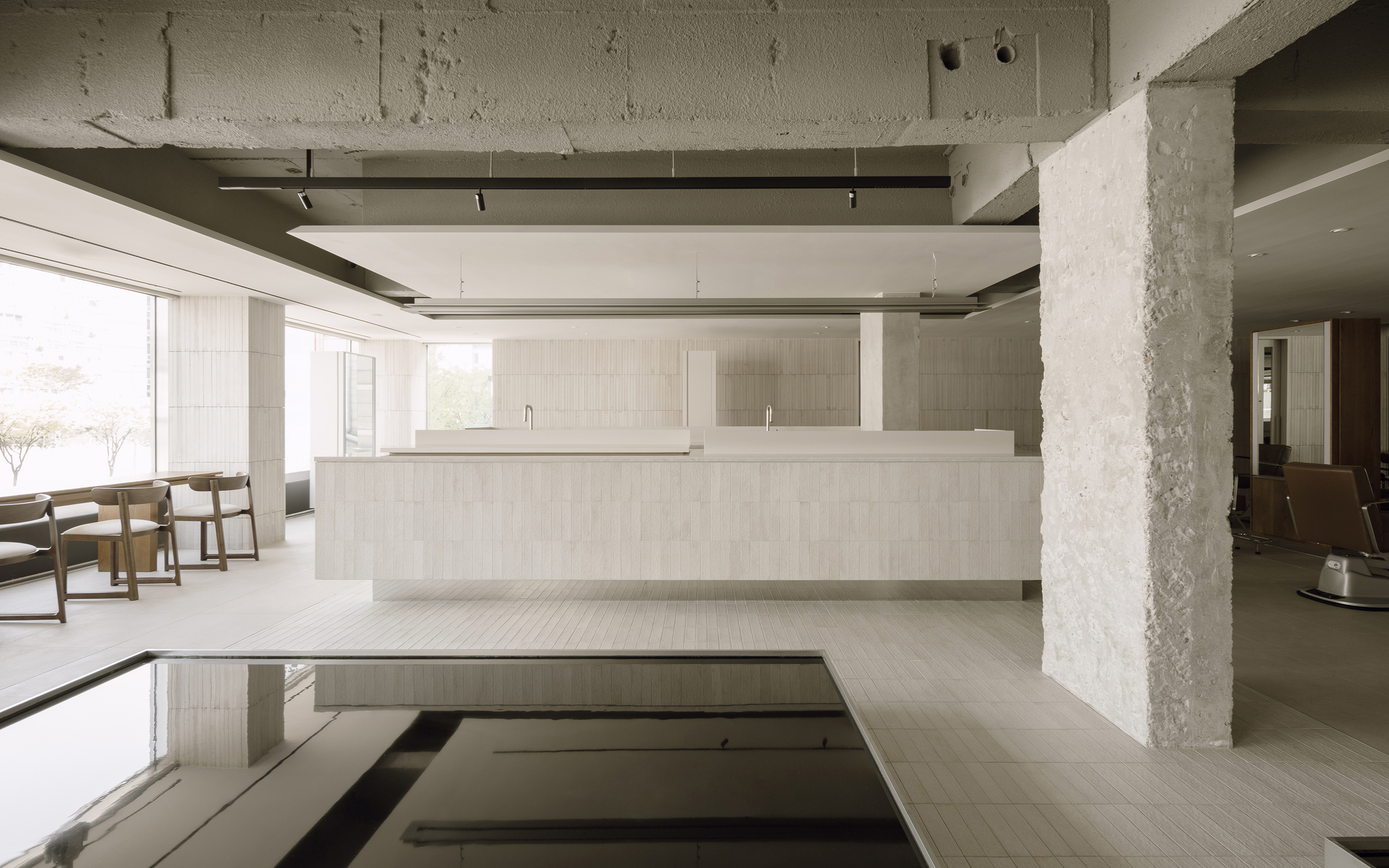 Salon interior with exposed concrete ceiling beams and recessed floor basins beneath pale tiled counters