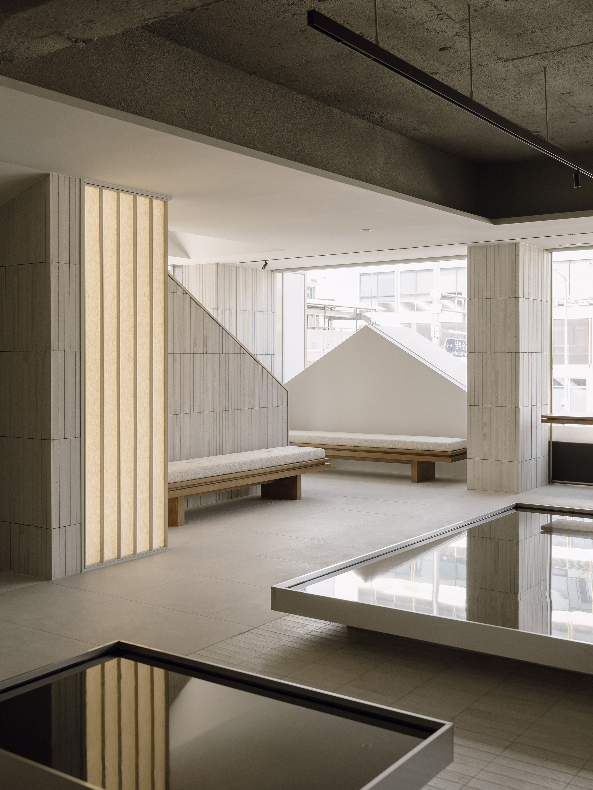 Seating niche with vertical fluted wall panel and timber benches beside mirrored floor inset