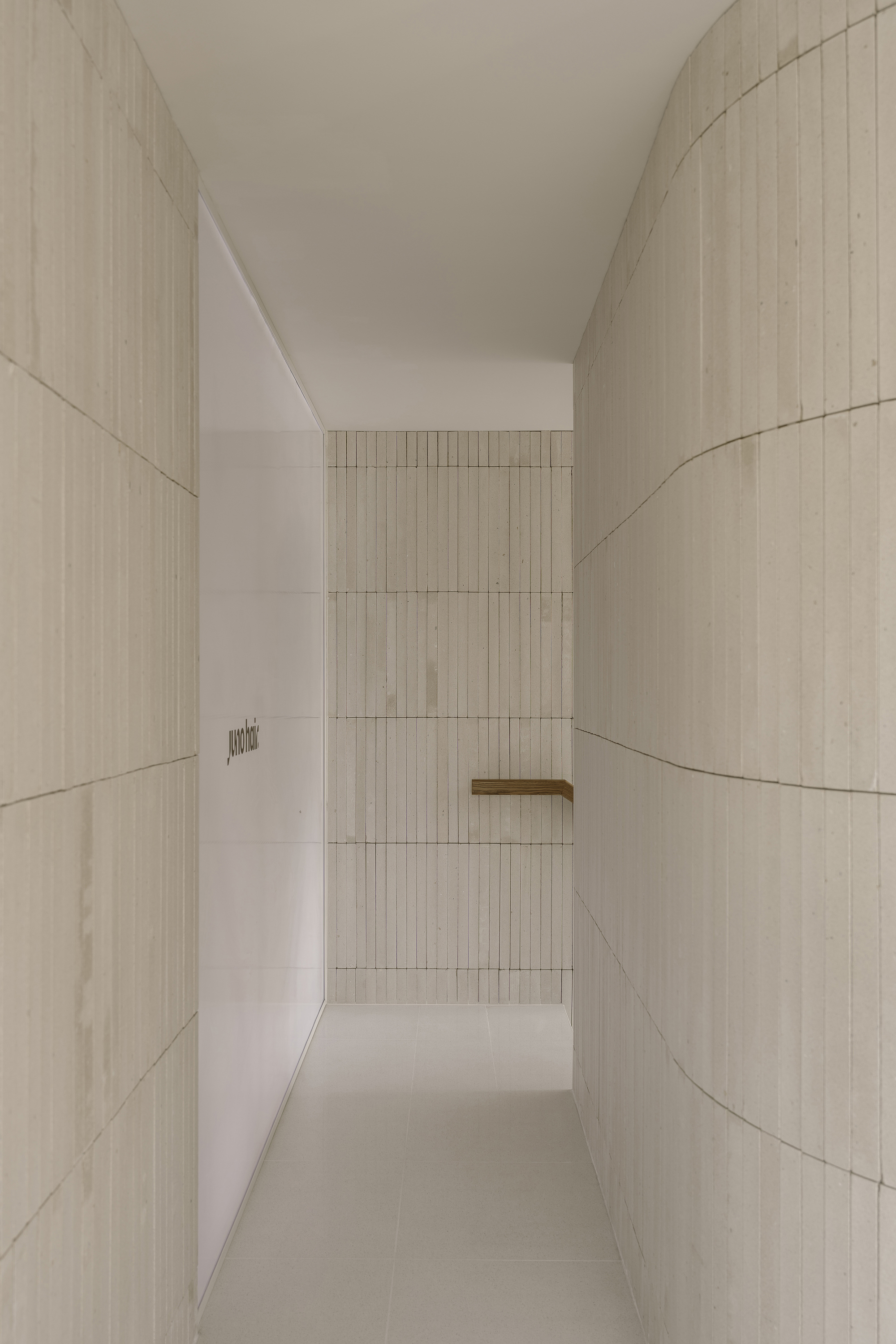 Narrow corridor flanked by curved ribbed tile walls leading to distant timber handrail