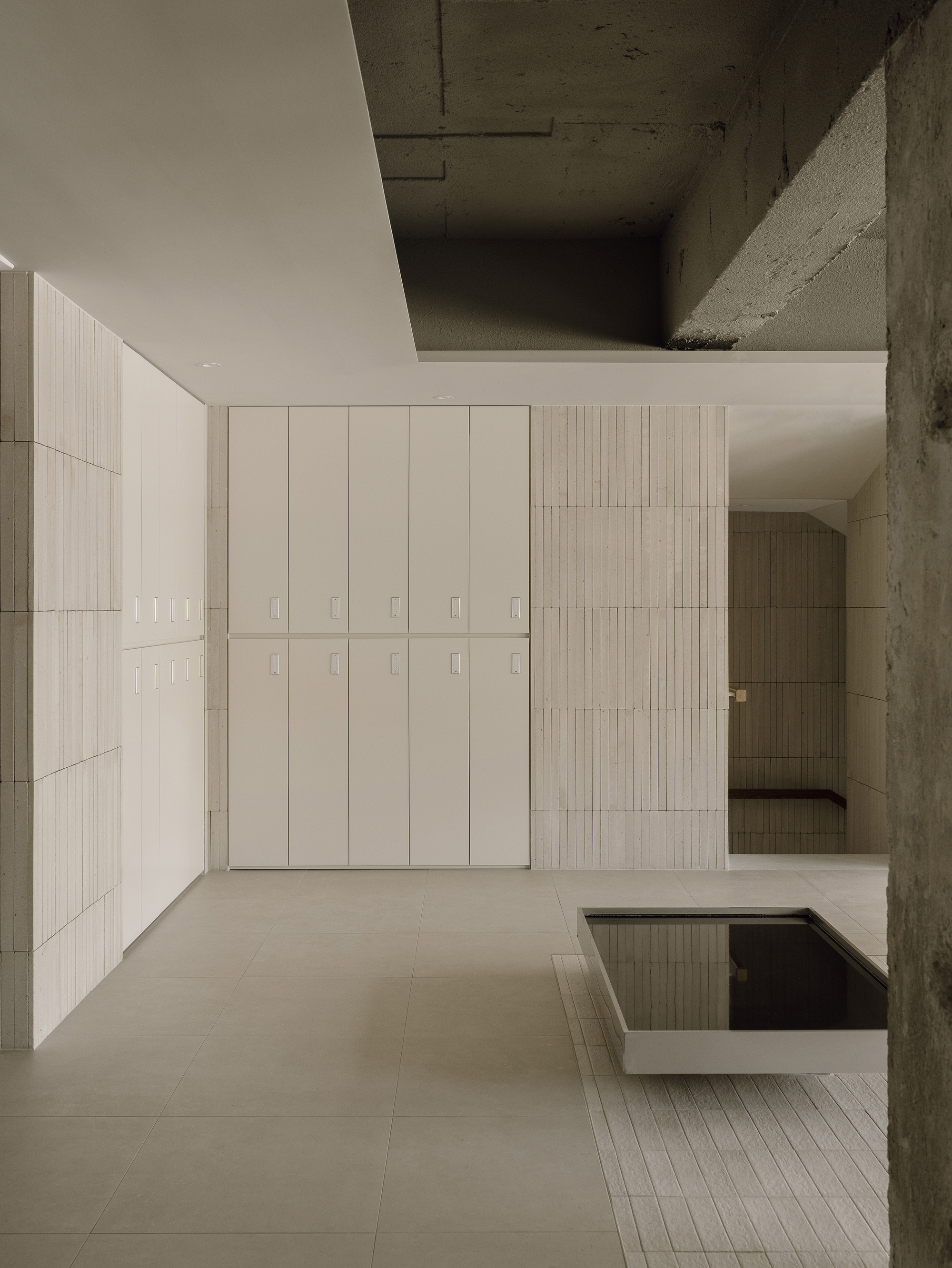 Interior view of pale tiled walls and exposed concrete ceiling framing a double-height salon space