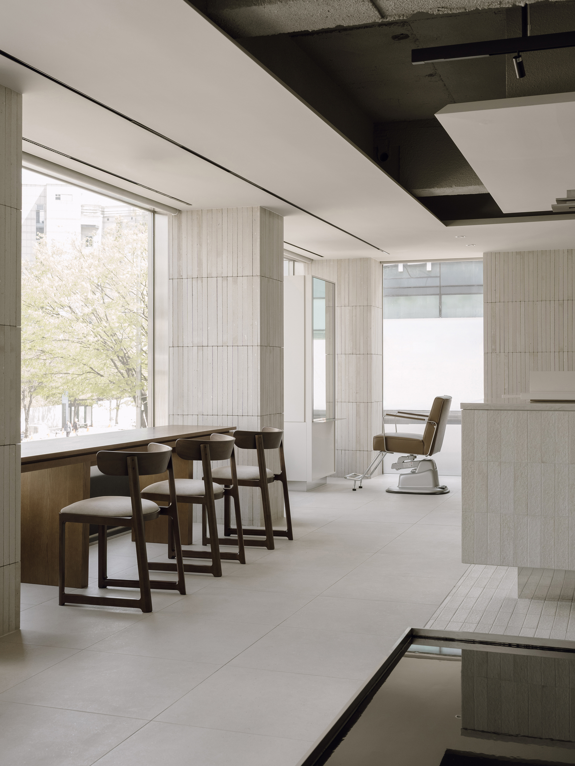 Row of wooden salon chairs facing floor-to-ceiling windows with spring trees visible outside