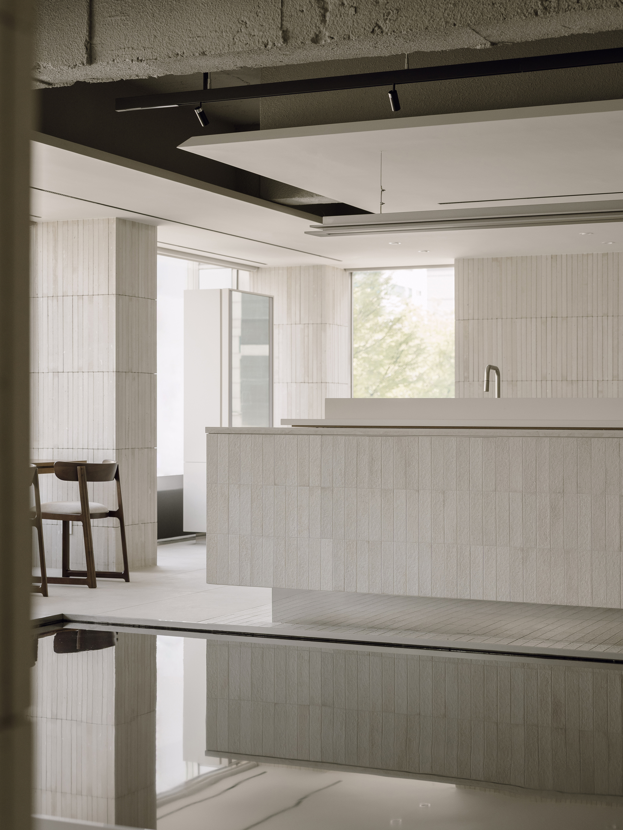 Salon workspace with light wood island and reflective dark water feature below exposed concrete beams