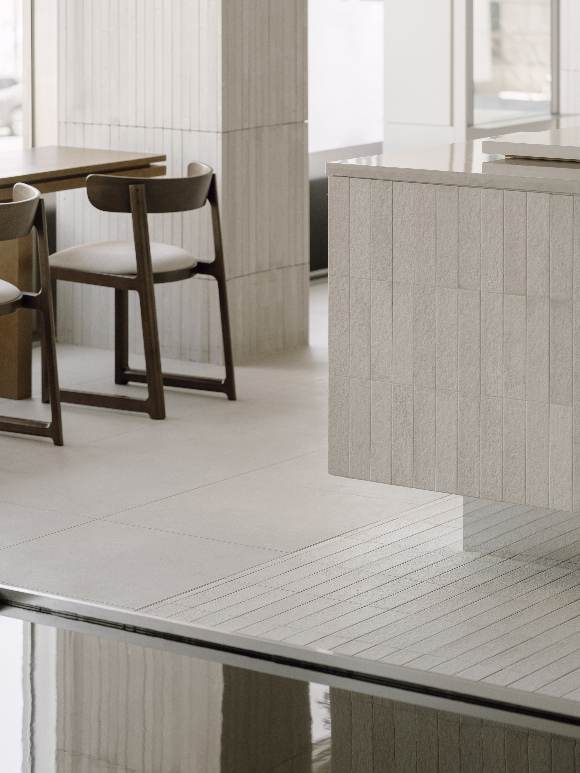 Detail of the junction between pale tiled salon counter and reflective dark glass surface