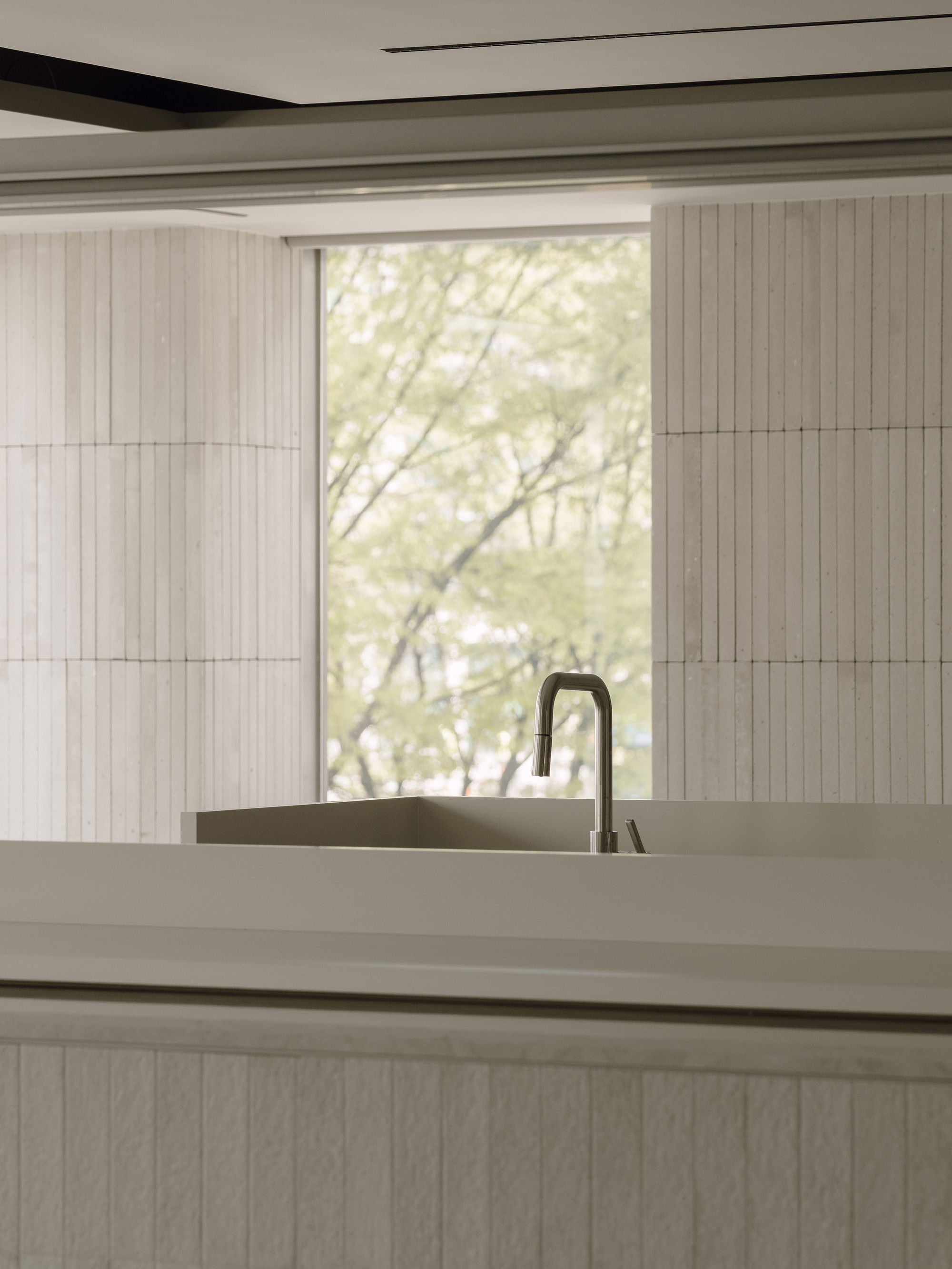 Kitchen island with integrated sink and tall faucet framed by vertical timber paneling and soft daylight
