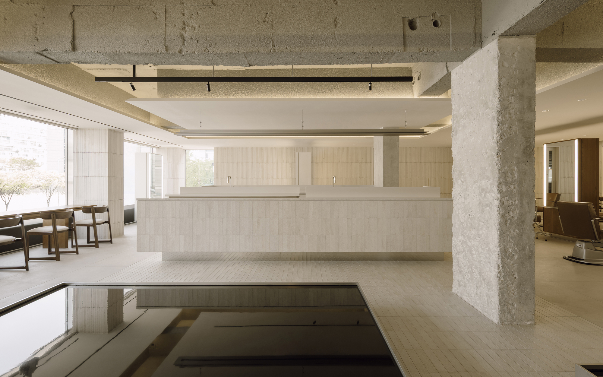 Reception desk with exposed concrete column and ceiling alongside a recessed floor pool reflecting overhead beams