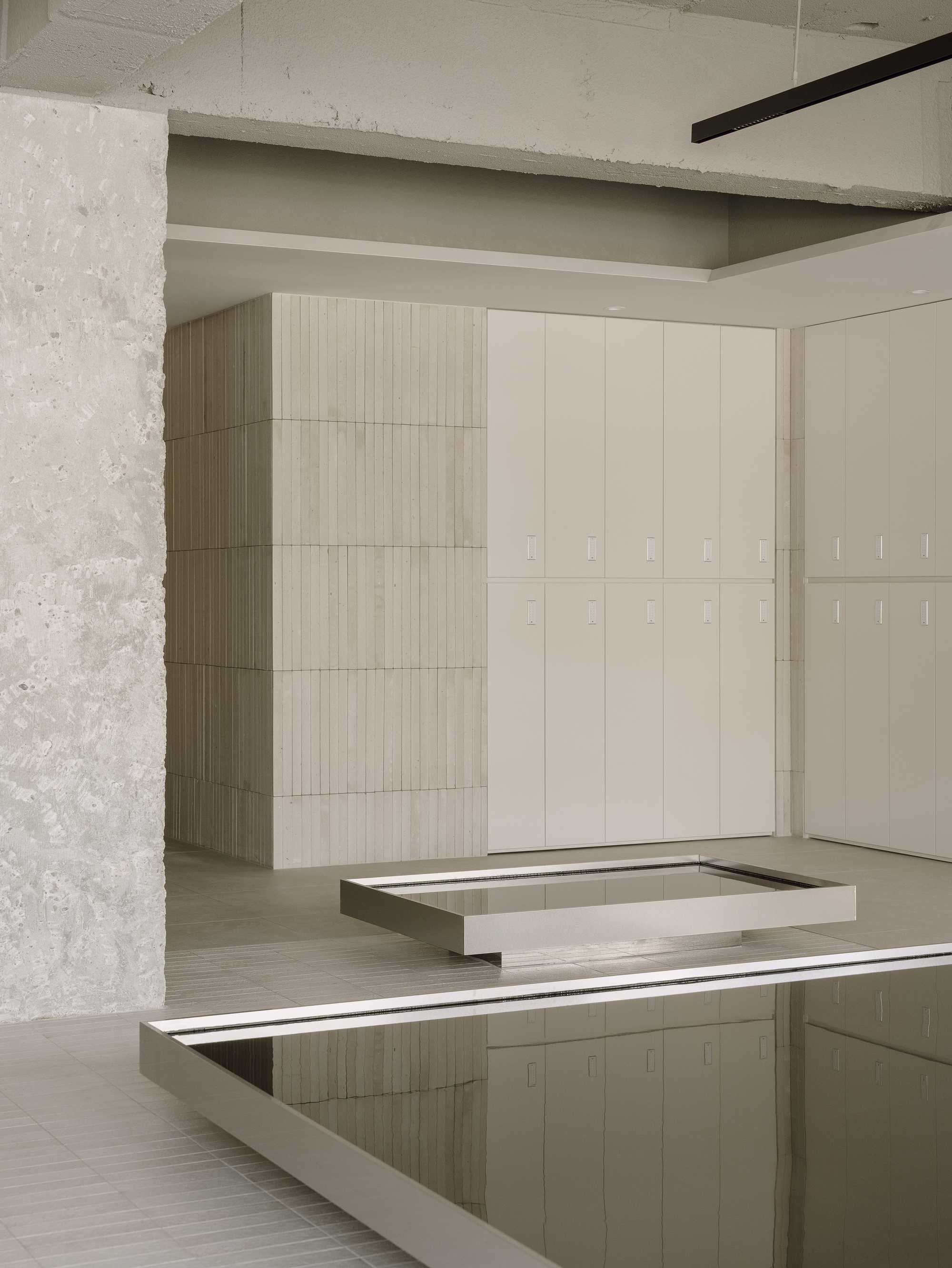 Pale timber locker wall next to concrete column with reflective pool edge in the foreground