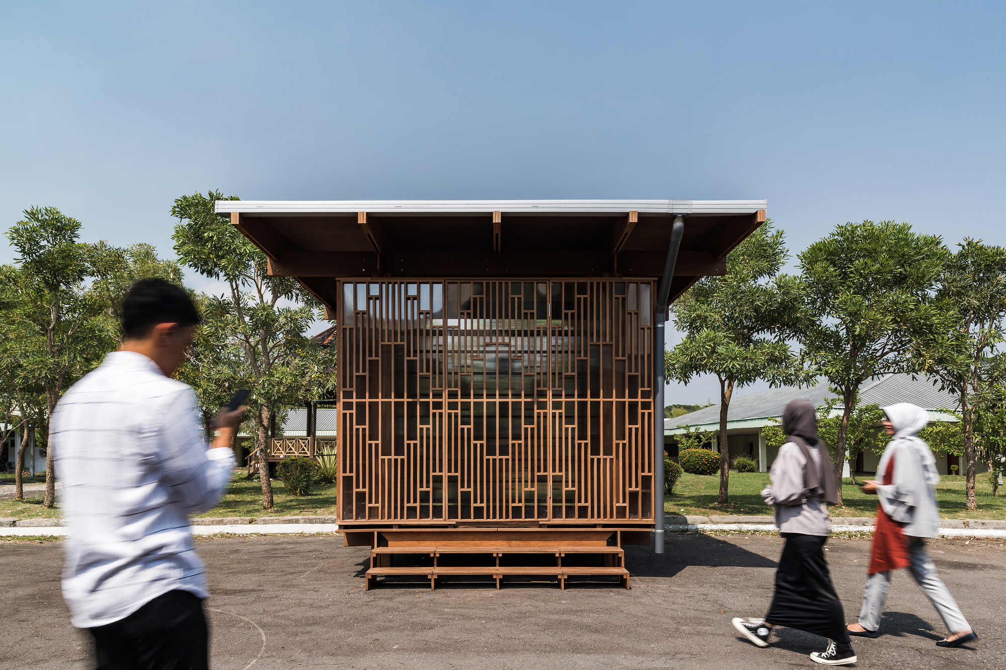Small timber pavilion with geometric screen facade and cantilevered roof as pedestrians pass by