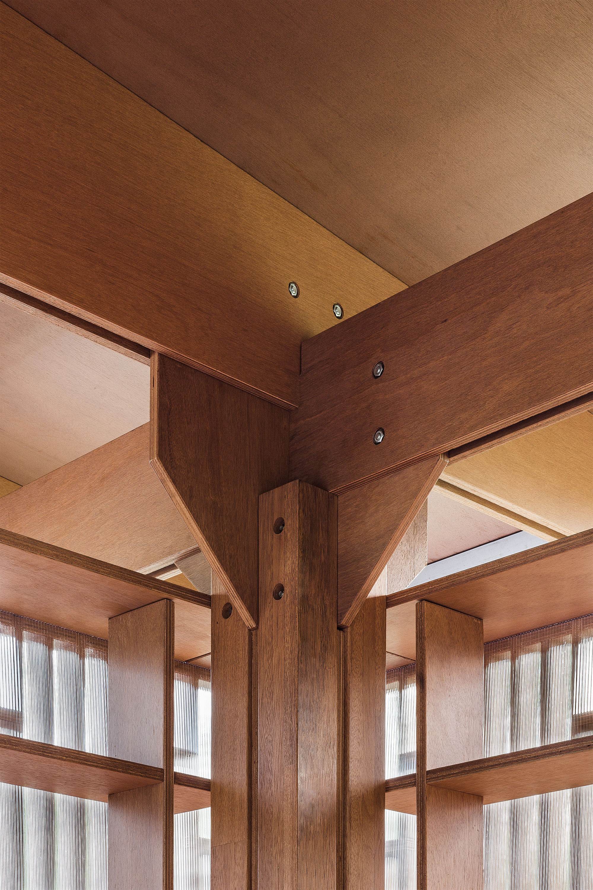 Detail of timber structural column and beam intersection with visible bolted connections and plywood ceiling