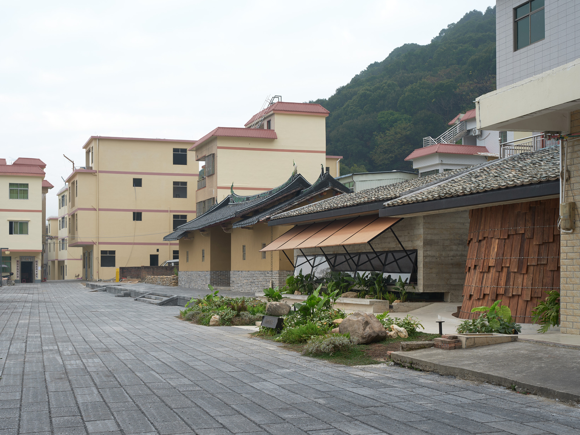 Curved gabled roof structure with timber shingles and planted beds fronting a residential street