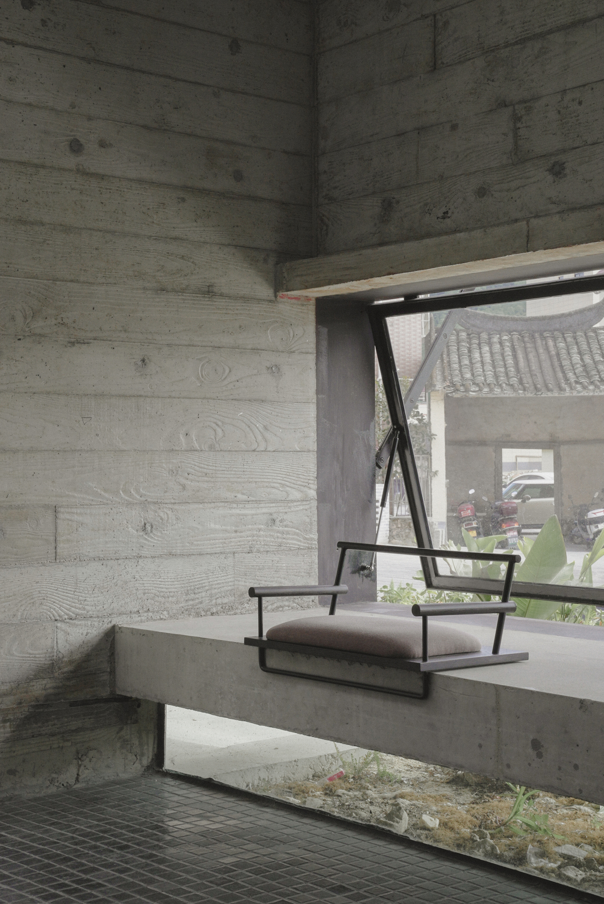 Concrete bench seat beneath board-formed walls and angled window framing planted courtyard beyond