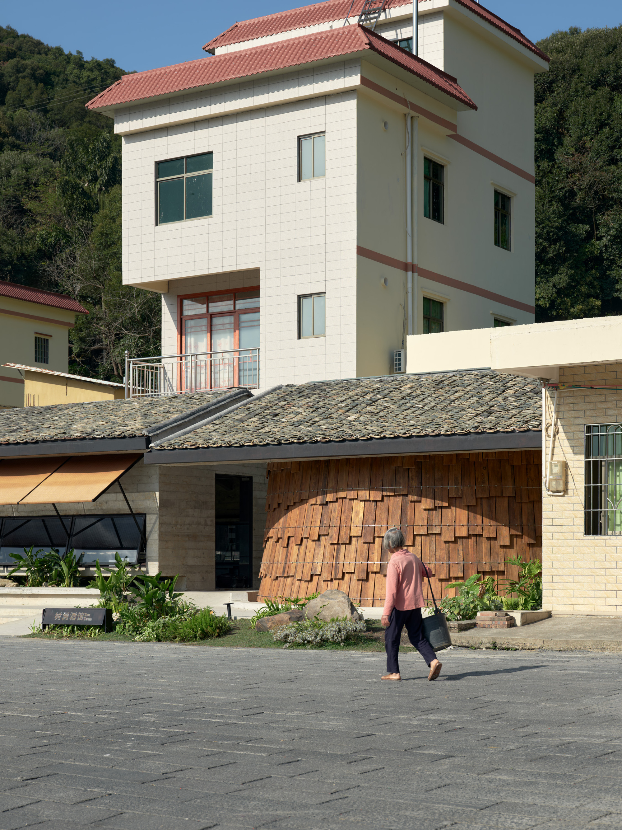 Arched timber screen facade with a person walking across the paved courtyard
