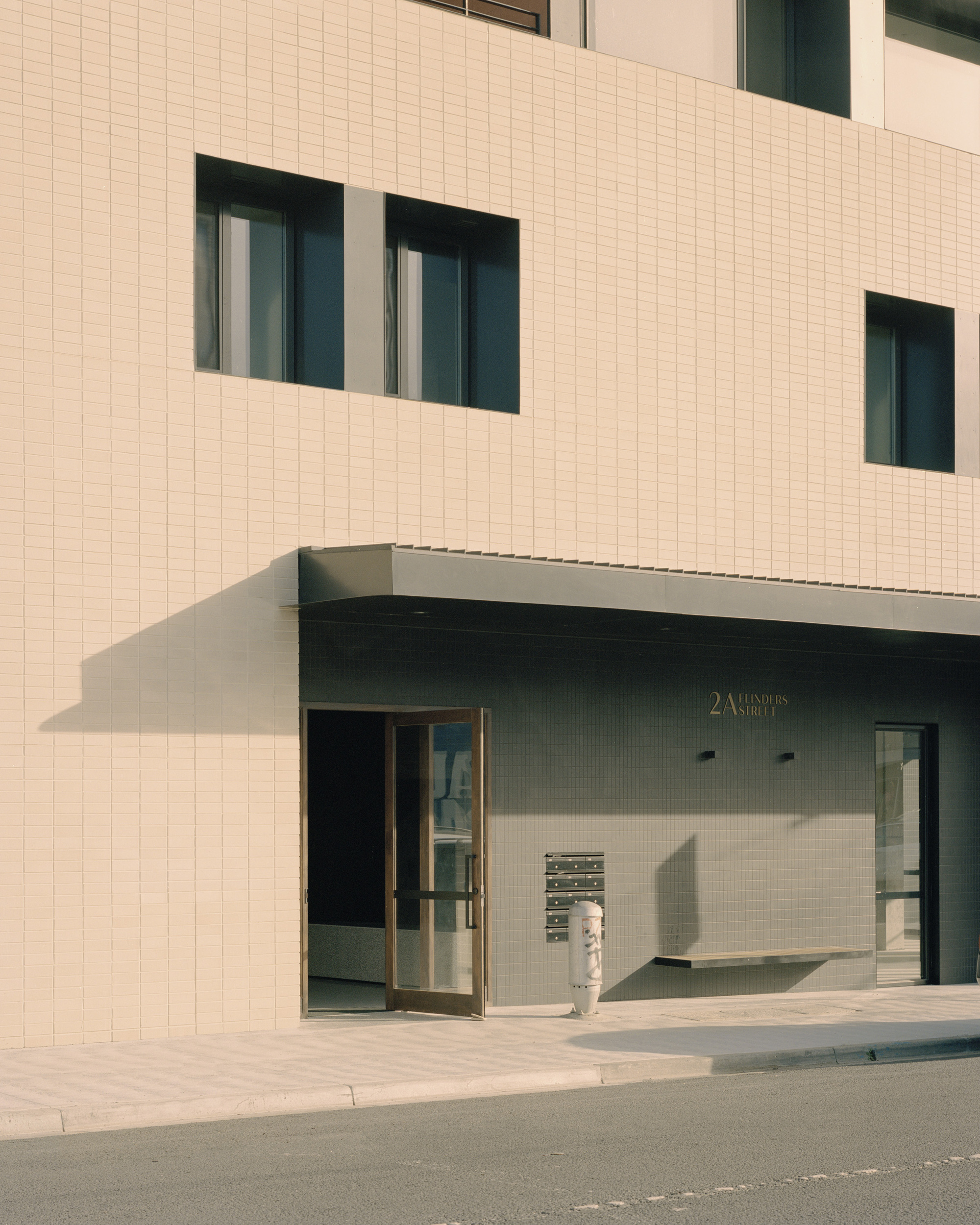 Ground-level entrance with recessed glazing and a canopy cutting into the tiled facade in afternoon sun