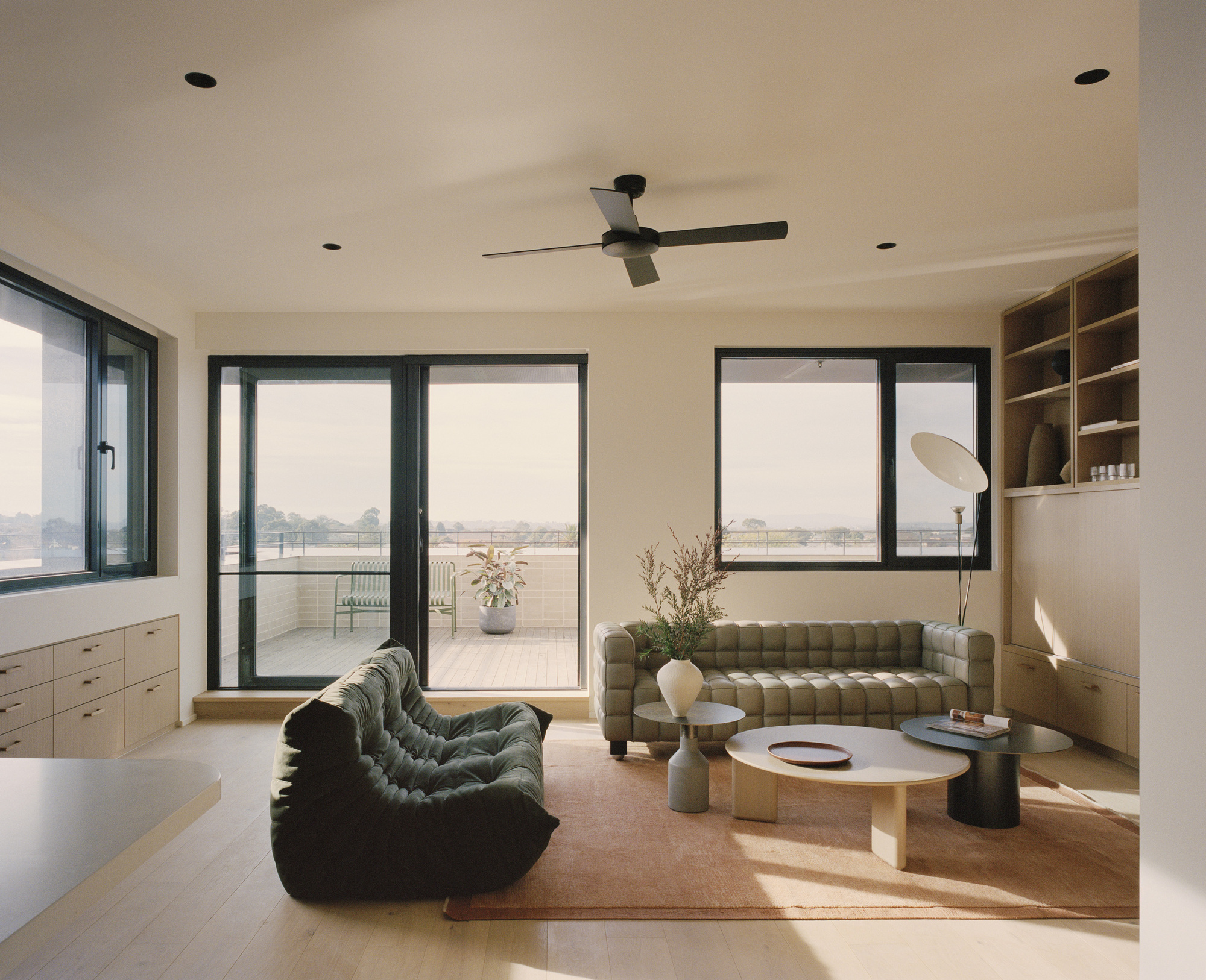 Living room with dark-framed sliding doors opening to a terrace and built-in timber shelving at right