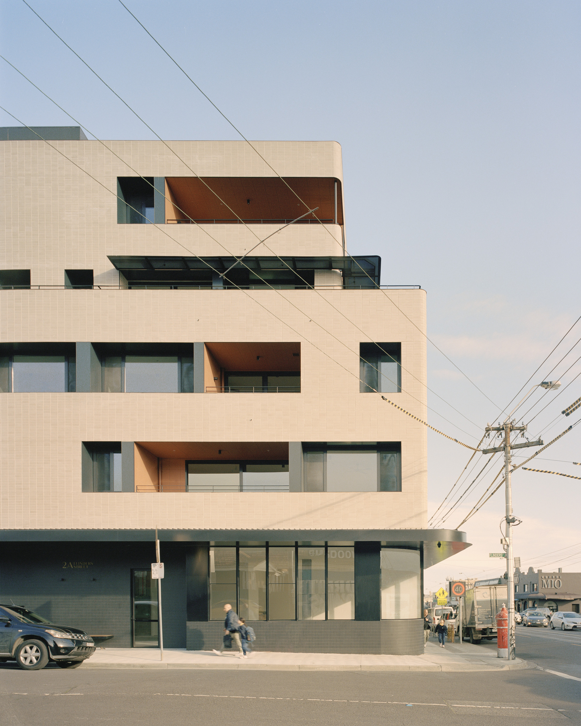 Street view of the light tile facade with recessed terraces and overhead power lines
