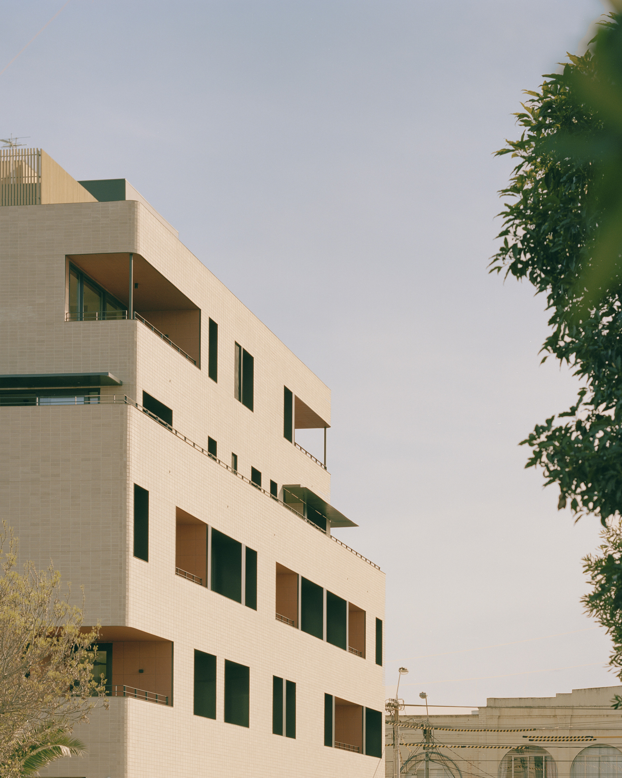 Upper floors of the cream tile facade with staggered terraces framed by foliage
