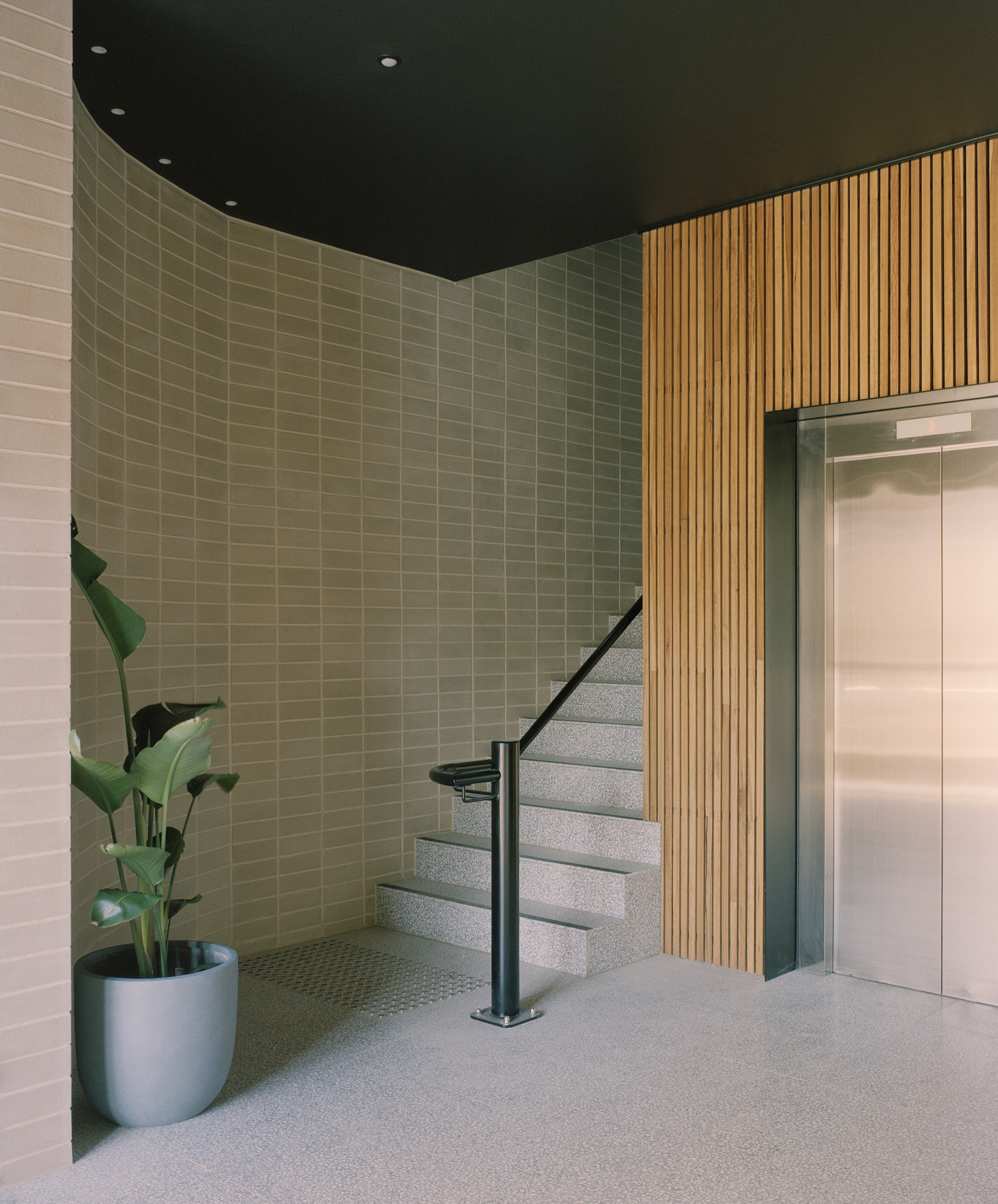 Ground floor lobby with terrazzo stair, vertical timber slats and potted plant
