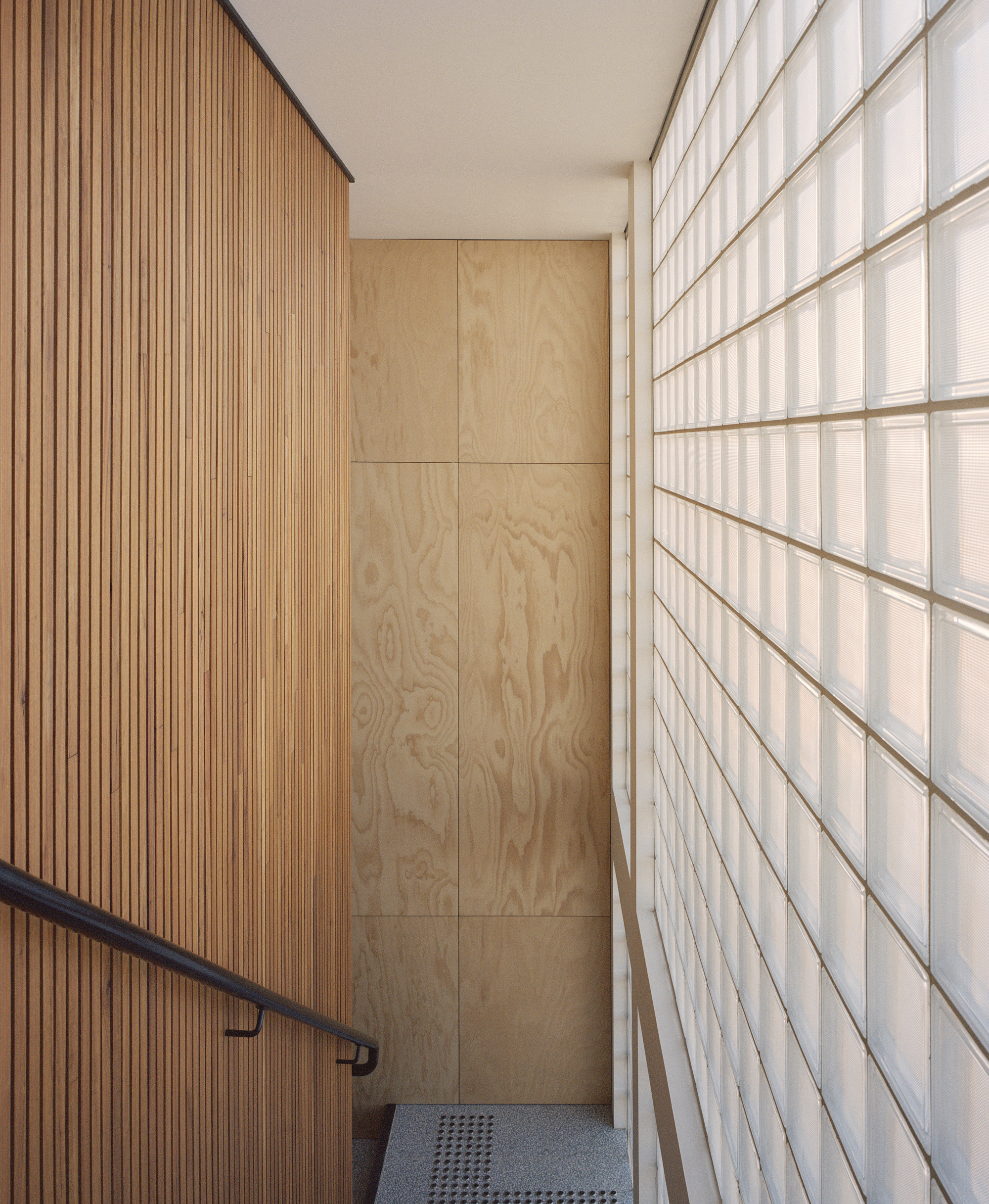 Narrow stairwell with timber slat wall and translucent glass block partition