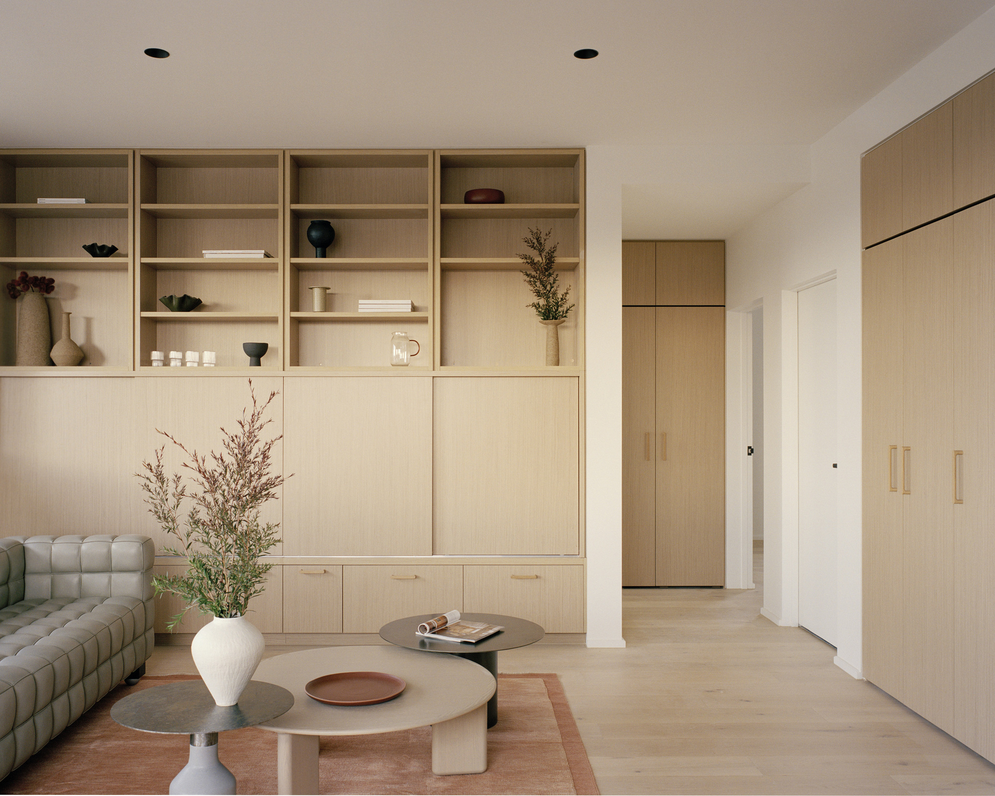 Living room with built-in pale timber shelving and storage wall framing a hallway to adjoining rooms