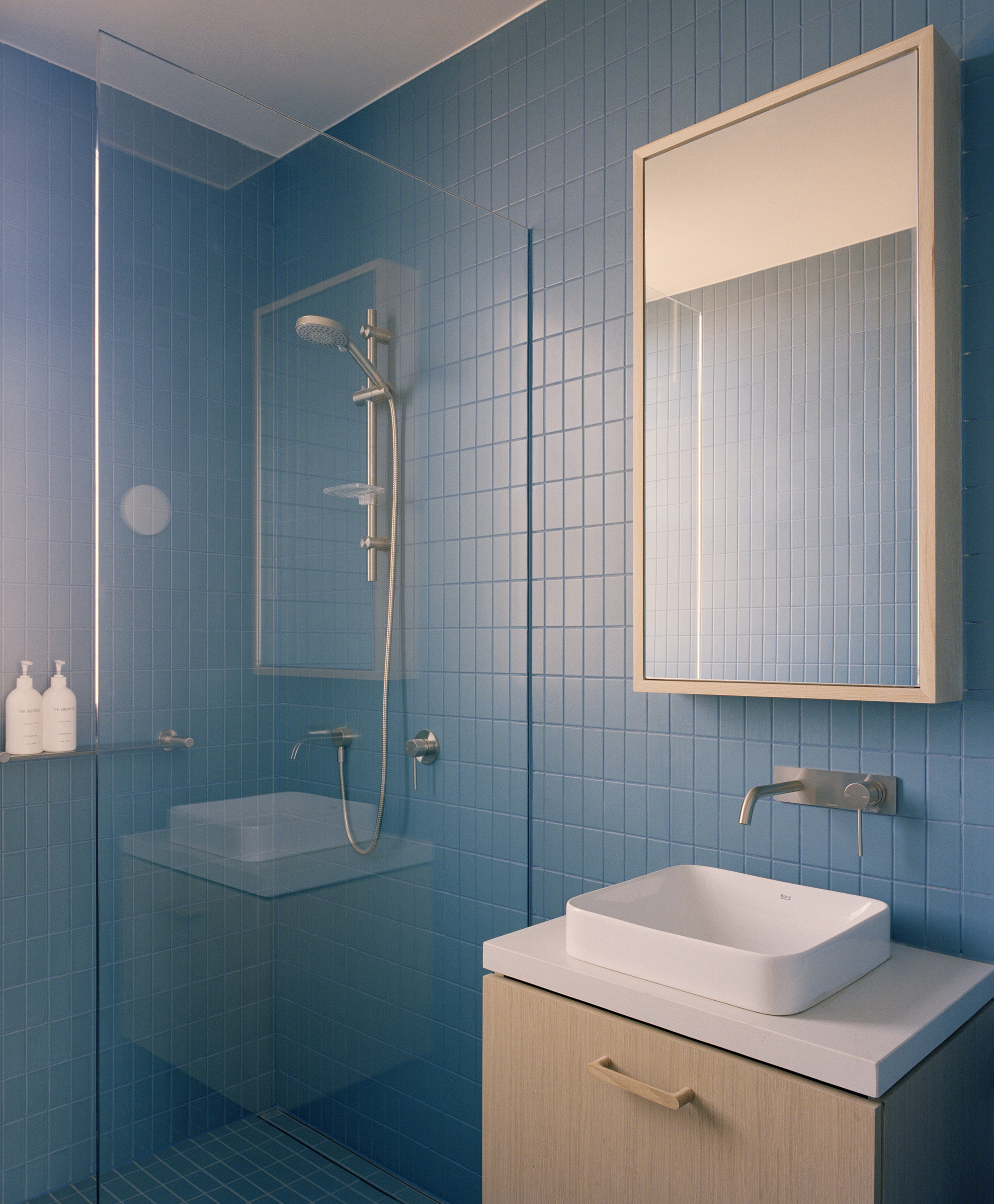 Bathroom with pale blue rectangular tile walls, glass shower enclosure and wall-mounted mirror cabinet