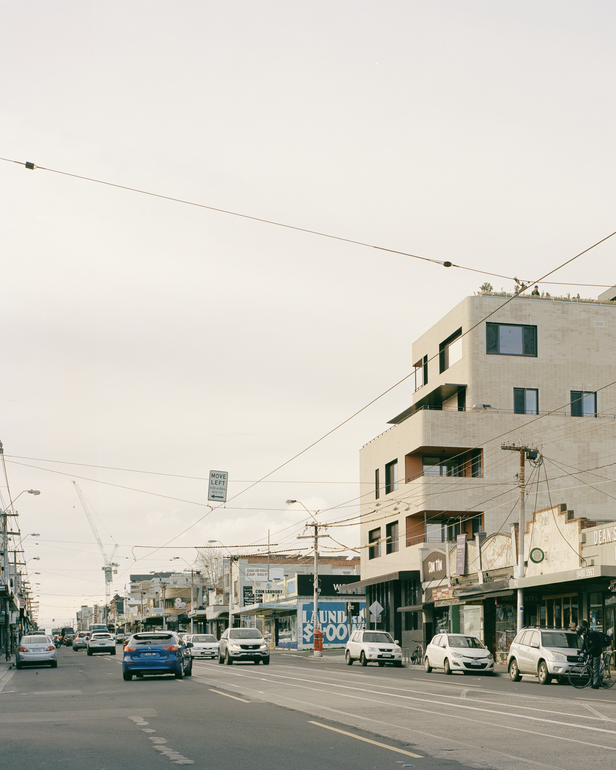 Stepped concrete facade on a corner site amid overhead tram wires and street traffic