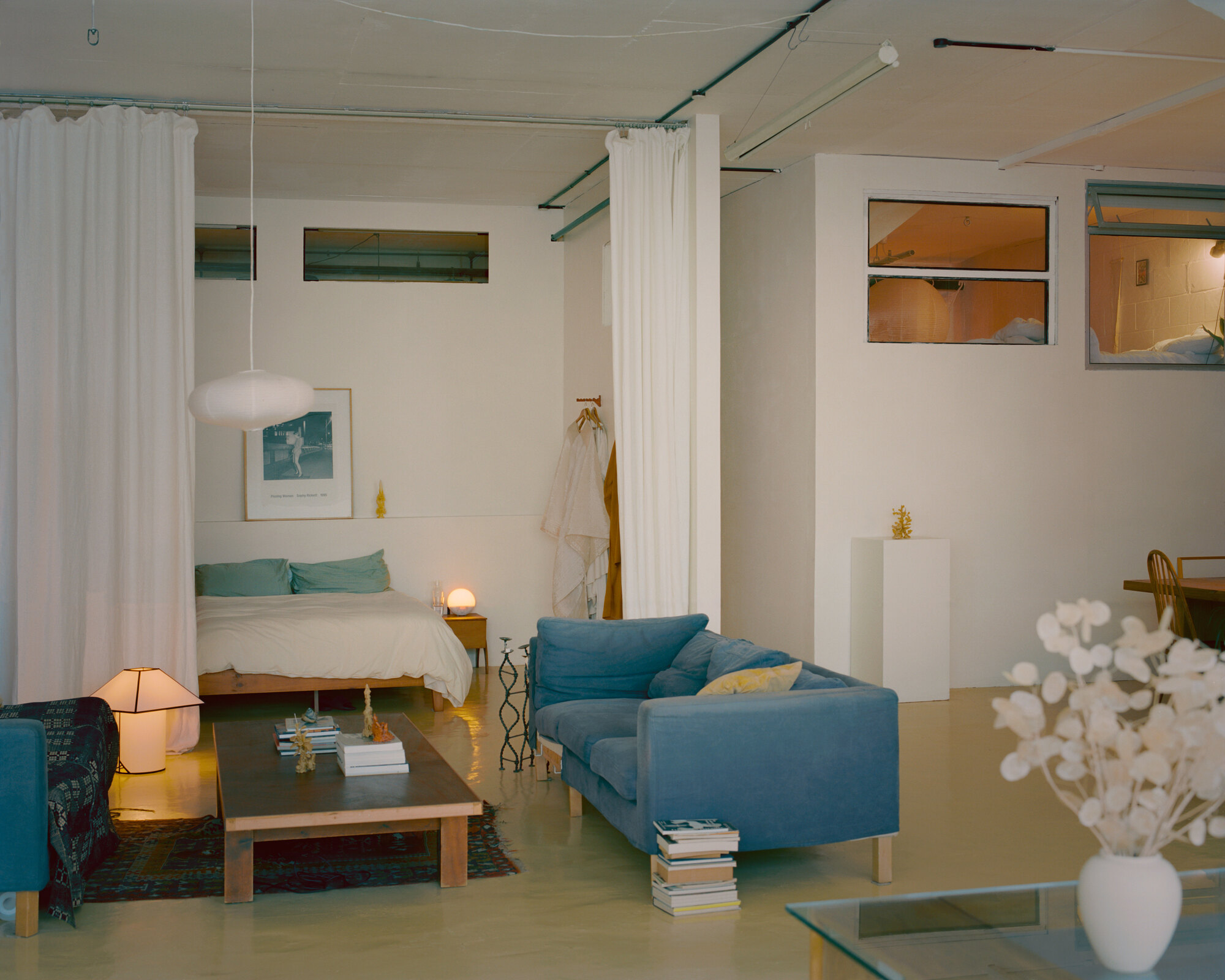 Open-plan living space with white curtain room dividers and clerestory windows at dusk