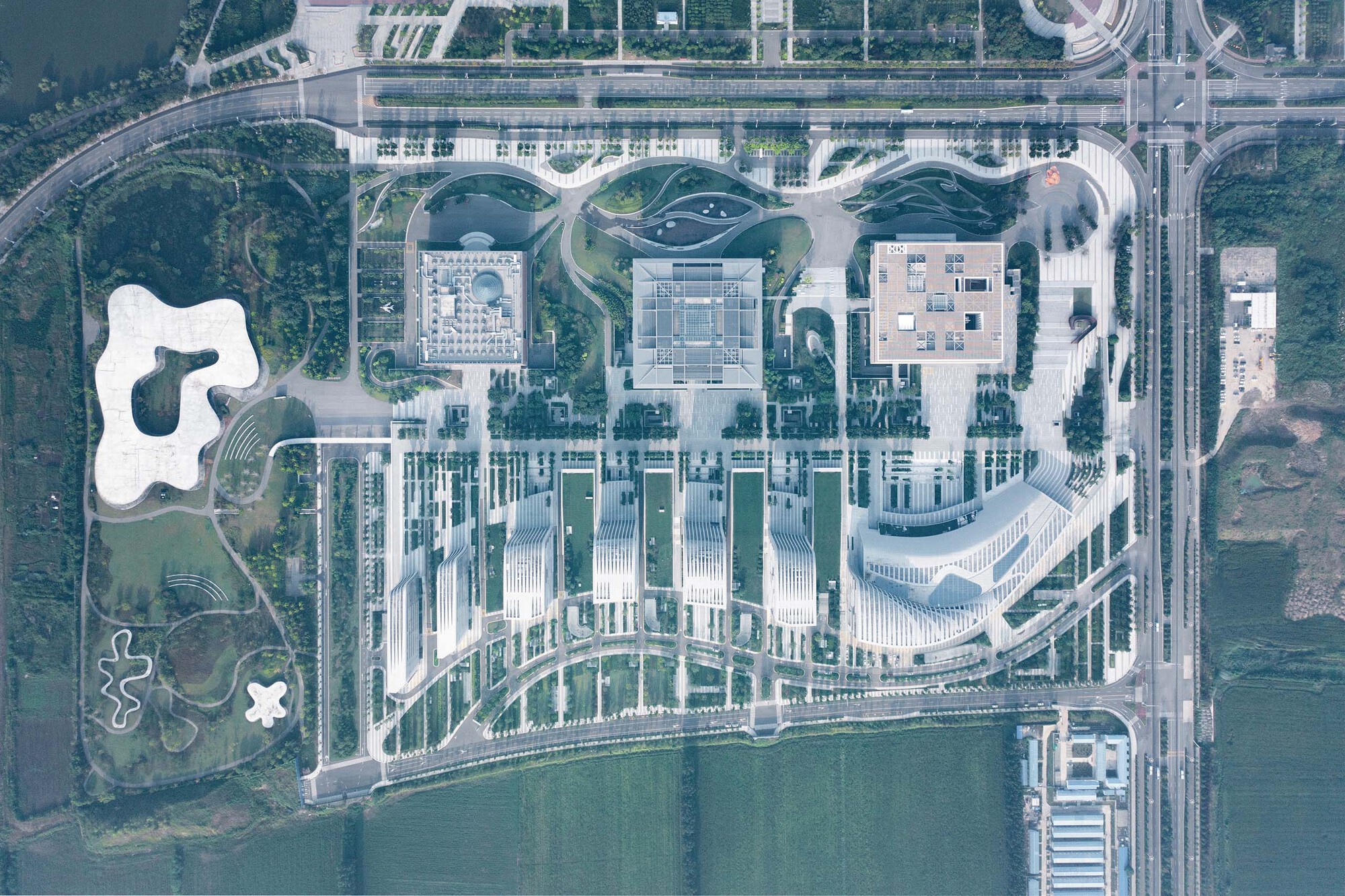 Aerial view of a campus with white ribbed towers and three organic-shaped roofs beside a waterfront
