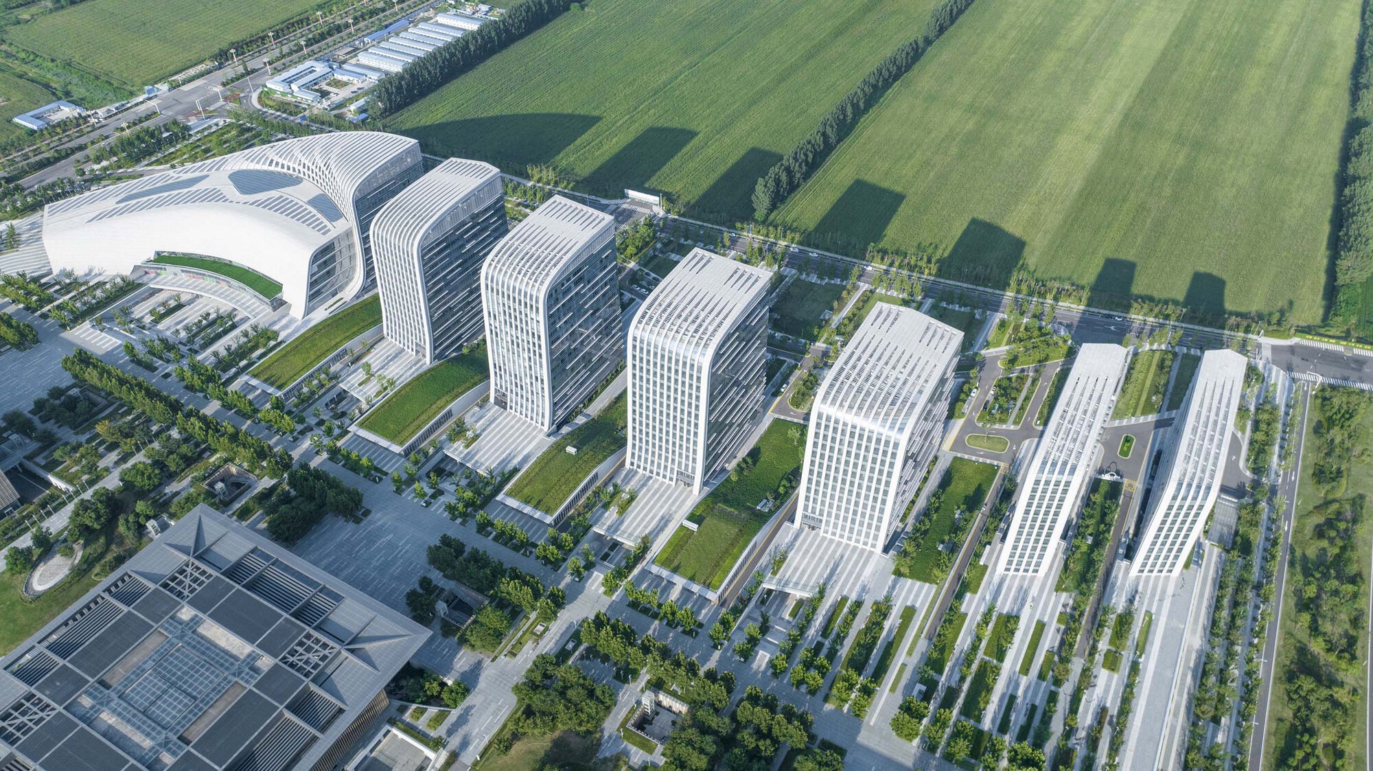 Aerial view of seven white-ribbed tower blocks arranged in two rows across landscaped grounds and green fields